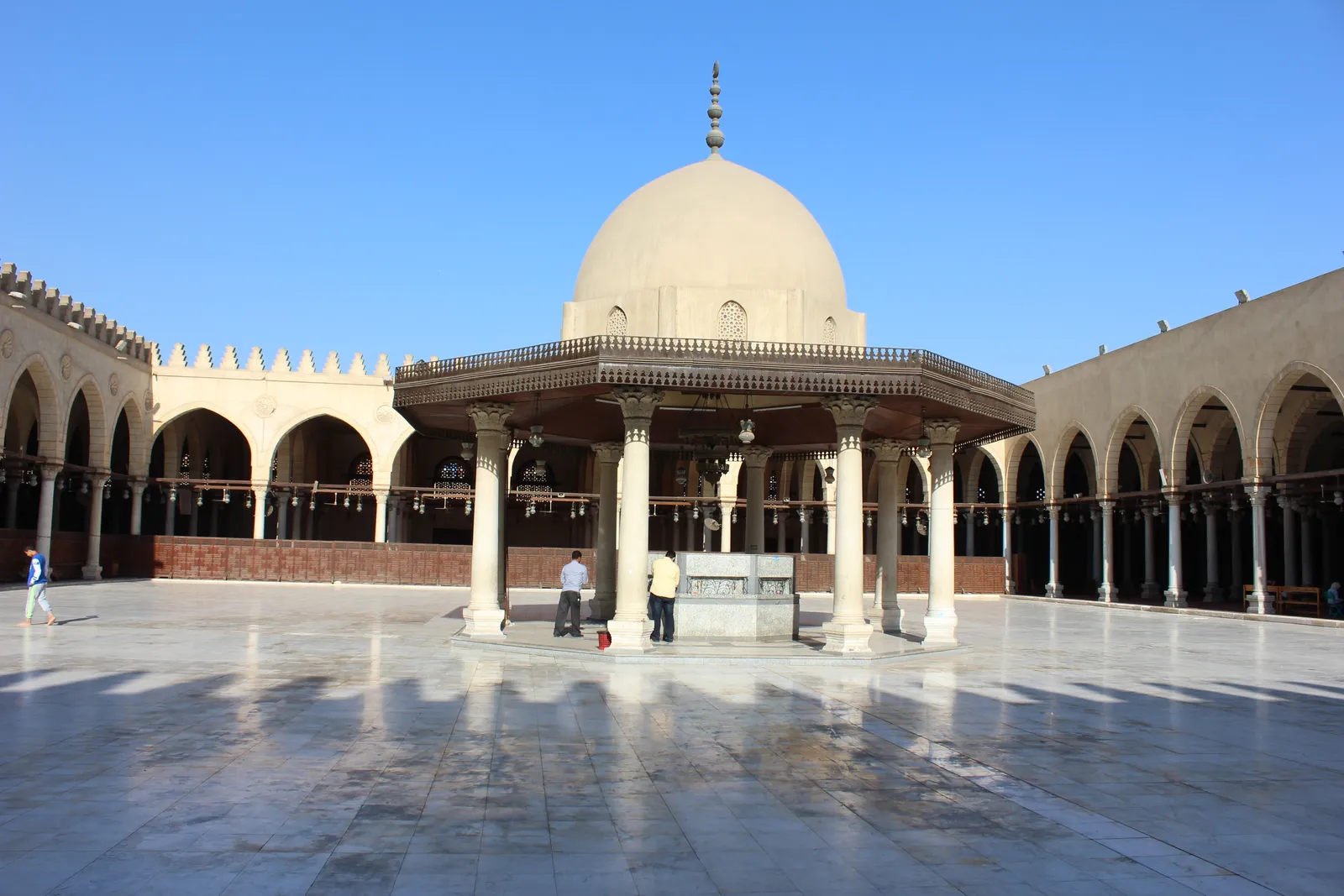 The courtyard of the mosque of Amr ibn al-As in Cairo, an open expanse of pale paving with a domed ablution pavilion in the centre and arcaded prayer halls running down both sides