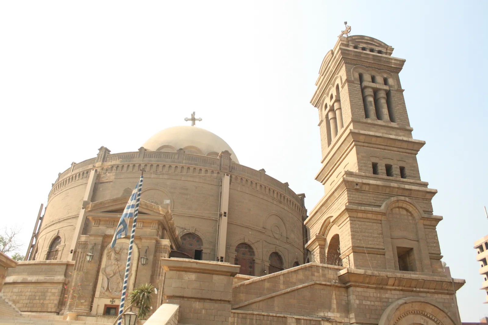 The Greek Orthodox church of St George in Old Cairo, a circular stone drum under a pale dome with a square bell tower attached at one side, seen from below against a bright sky