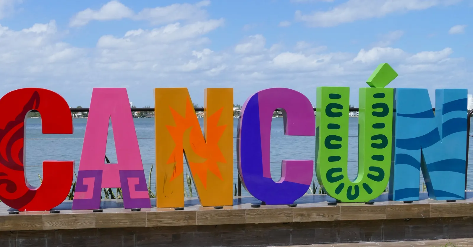 The painted block letters spelling Cancún at the El Mirador viewpoint, each one a different colour and carrying a different Maya-derived pattern, with the Nichupté lagoon behind them