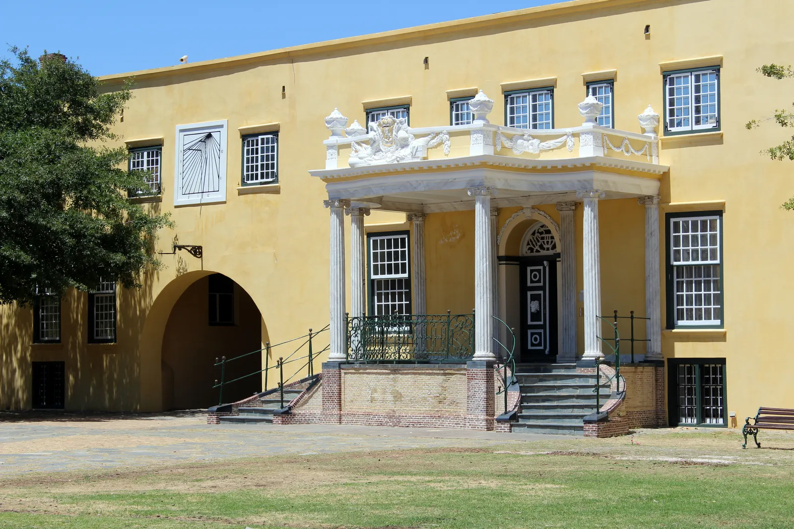 The Kat Balcony inside the Castle of Good Hope in Cape Town, a white columned portico with carved figures on its parapet and a double flight of steps, set against the castle's yellow-painted wall