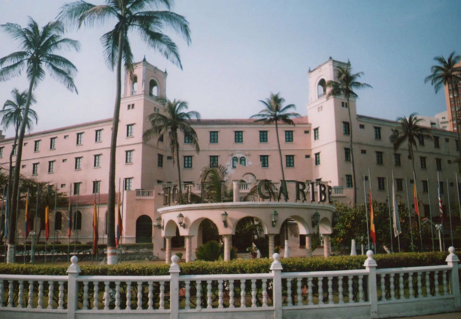 The pink colonial-tropical facade of Hotel Caribe in Bocagrande, Cartagena, with twin towers, palm trees and a curved entrance arcade