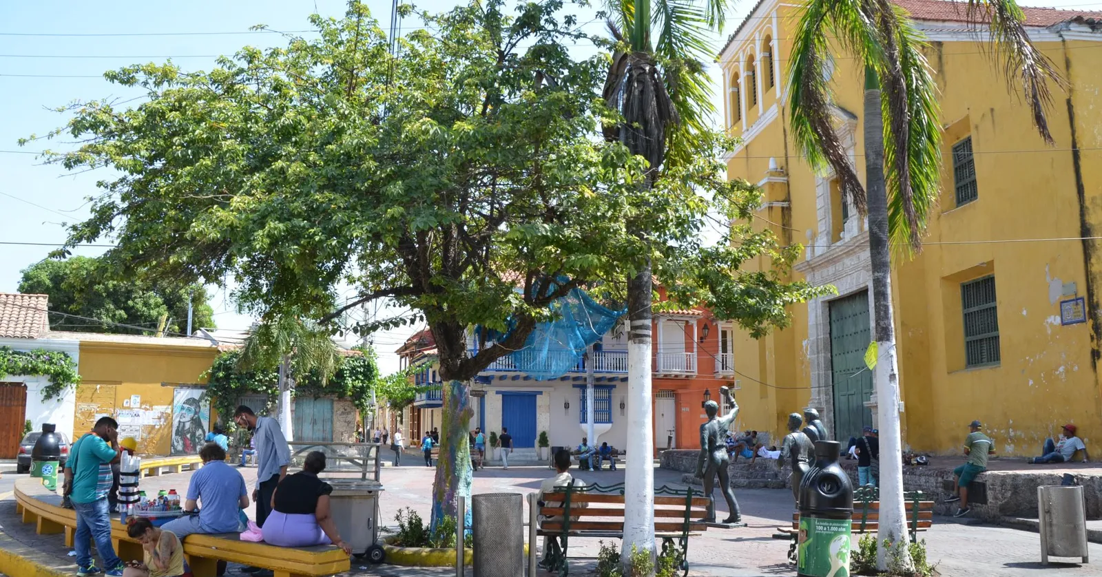 Plaza de la Trinidad in Cartagena's Getsemani neighborhood, with palm trees, benches and the yellow Iglesia de la Santisima Trinidad in the background
