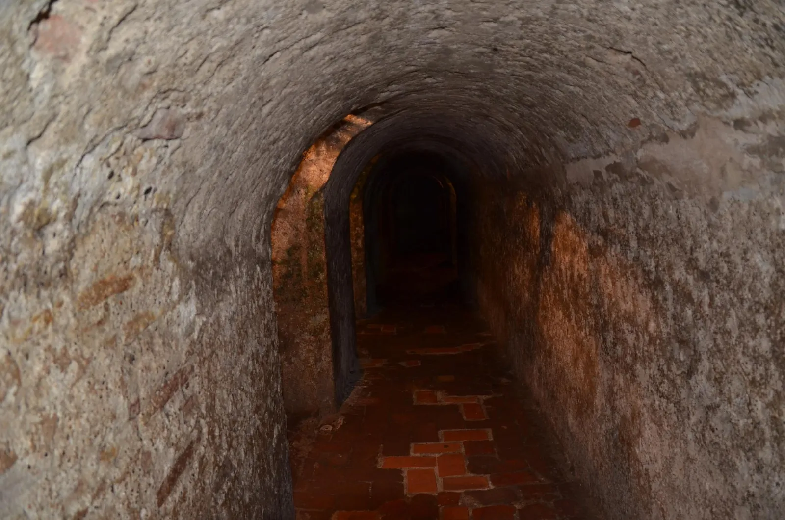 A dim, arched stone tunnel with a brick floor inside Castillo San Felipe de Barajas, curving away into darkness