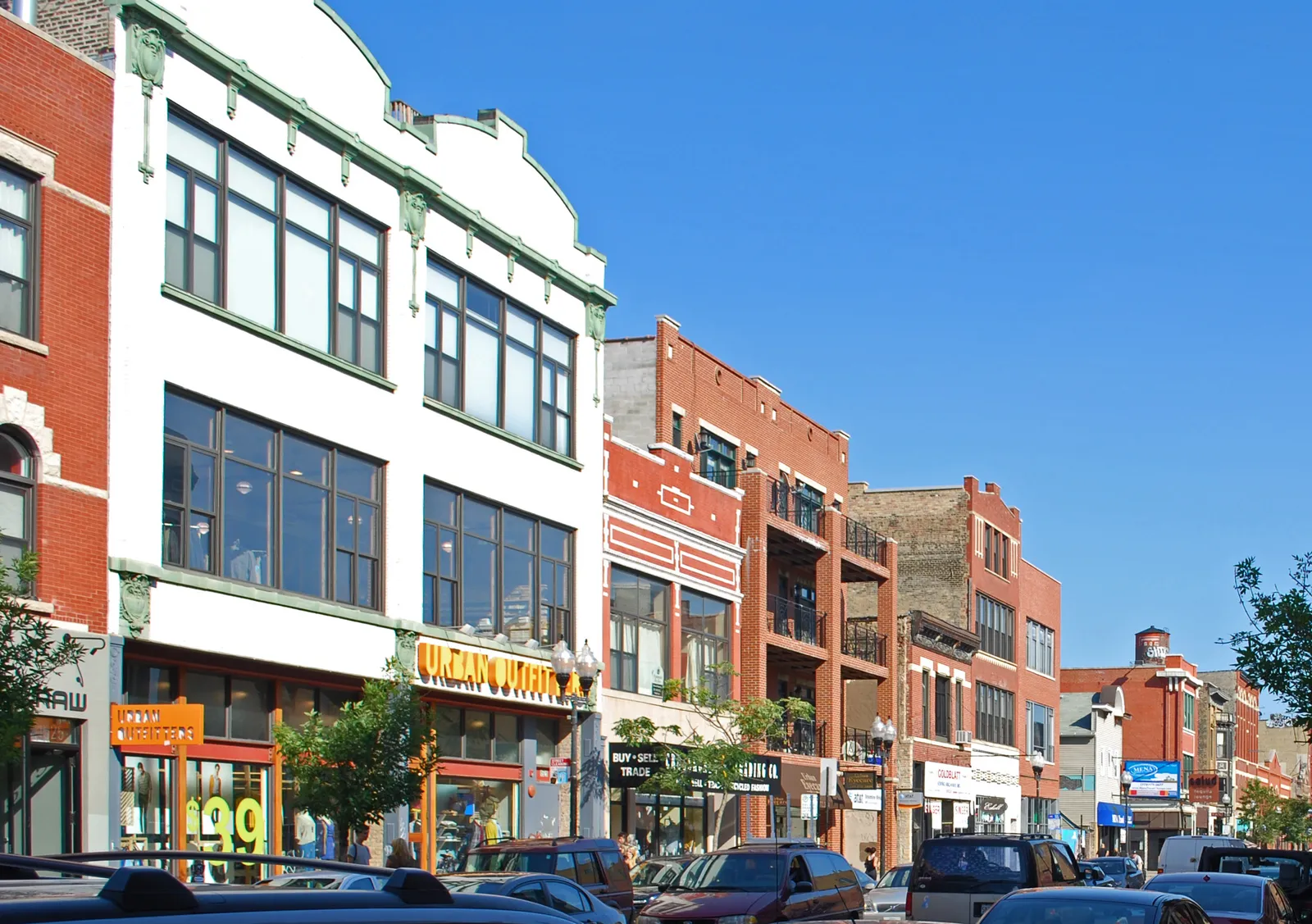 A row of two and three storey brick and terracotta shopfronts on Milwaukee Avenue in Chicago's Wicker Park, awnings and signs at street level under a clear sky