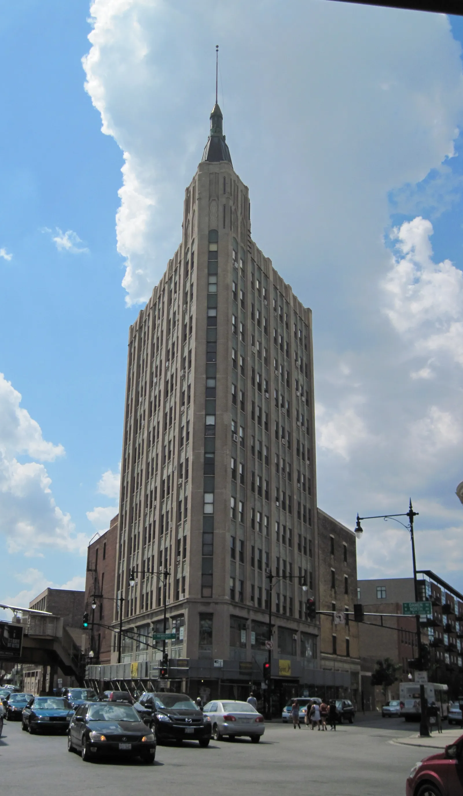The Northwest Tower in Chicago's Wicker Park, a narrow limestone Art Deco block rising to a stepped crown and a pointed spire, photographed from the street corner below