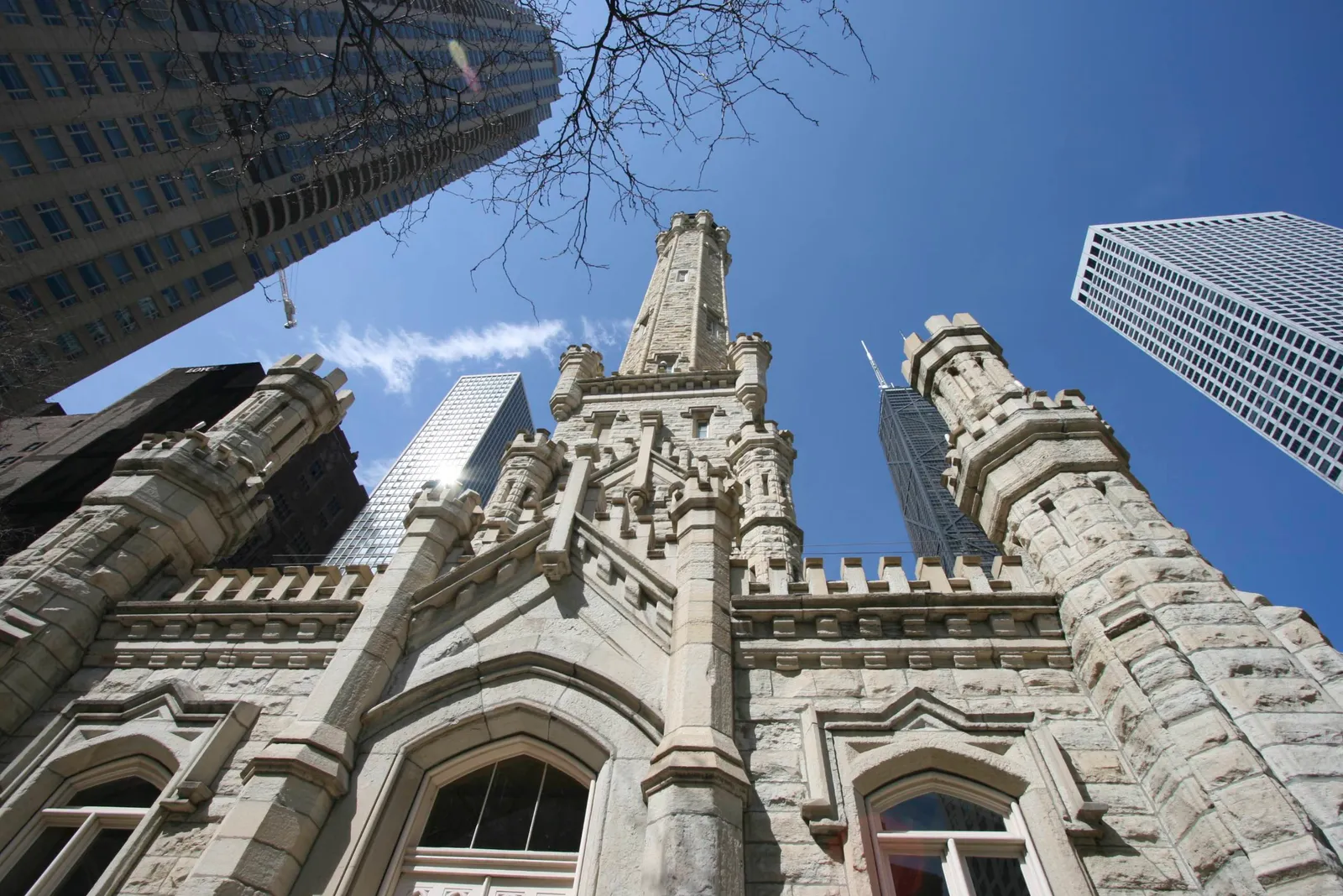 The Chicago Water Tower, a castellated yellow limestone tower with turrets and pointed windows, photographed from below with modern glass towers rising on every side of it
