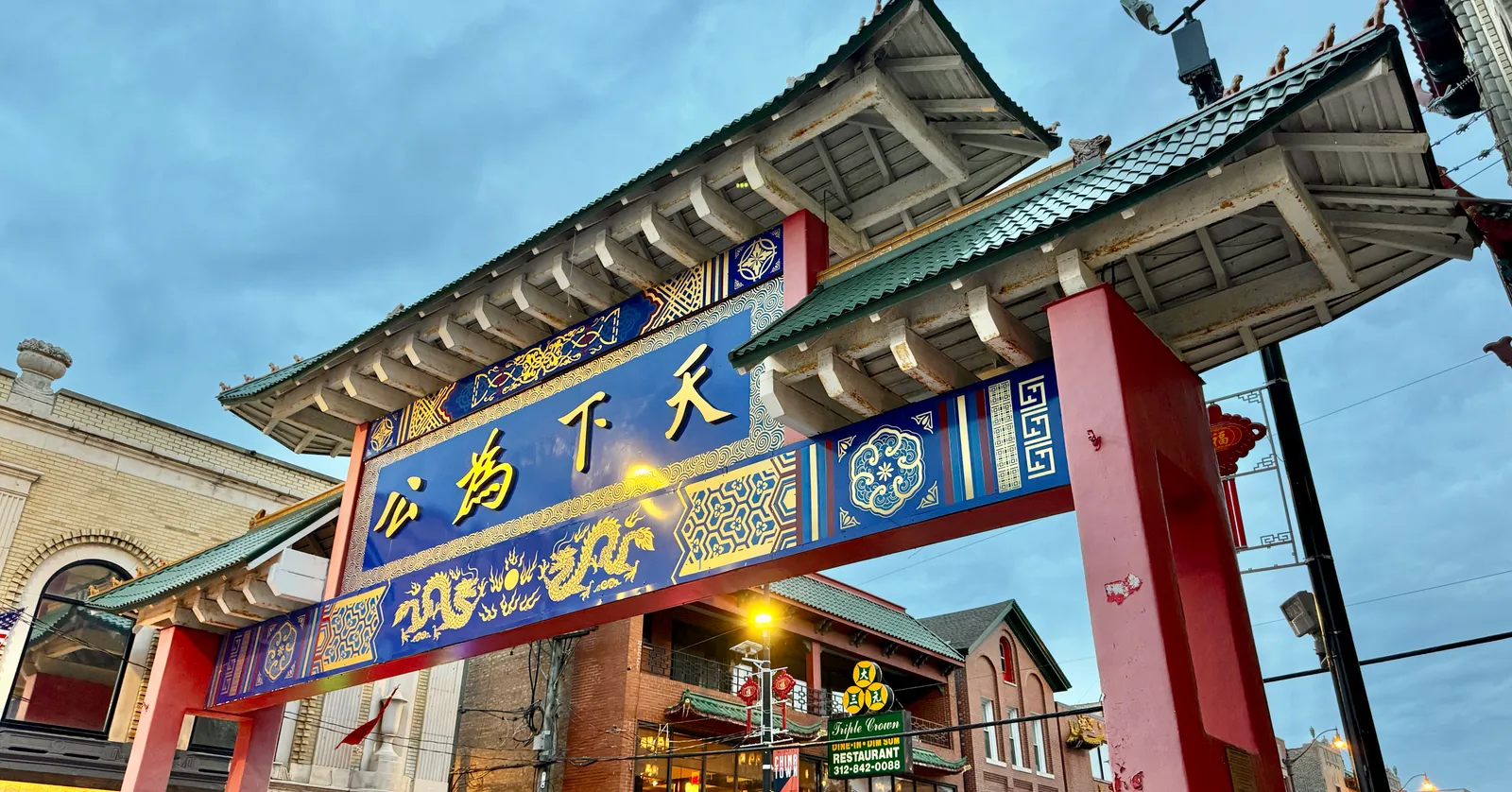 The Chinatown Gate over Wentworth Avenue in Chicago, a red and green tiled archway carrying four gold Chinese characters, photographed from below at dusk