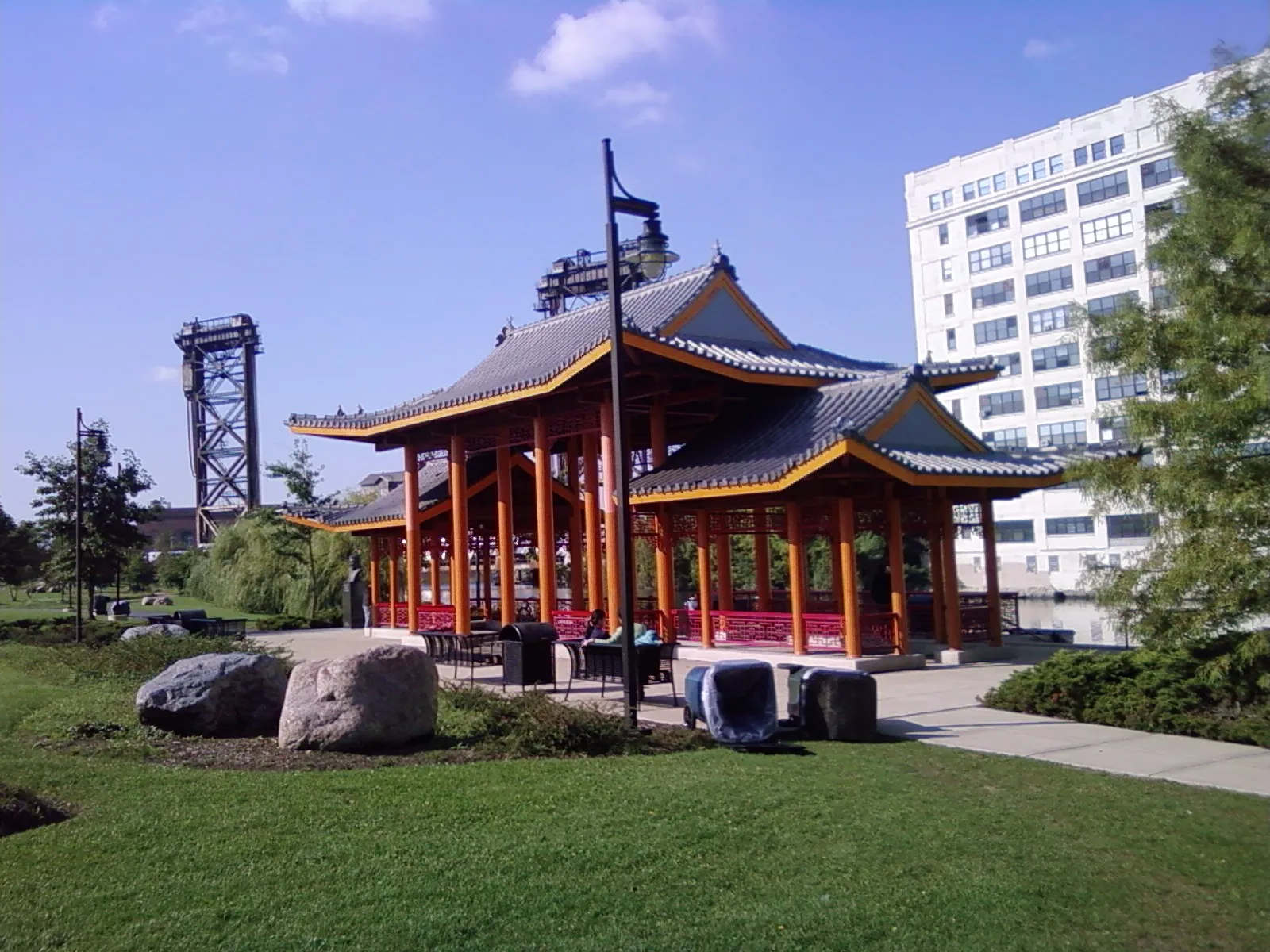 The red-columned pagoda pavilion in Ping Tom Memorial Park, Chicago, standing on a lawn with an old railroad lift bridge over the Chicago River behind it