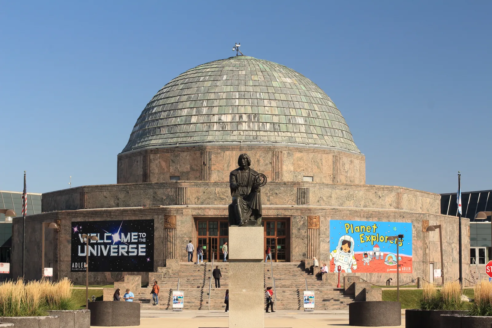 The Adler Planetarium in Chicago, a low granite drum under a weathered copper dome, with a bronze seated statue on a plinth in front of the entrance steps