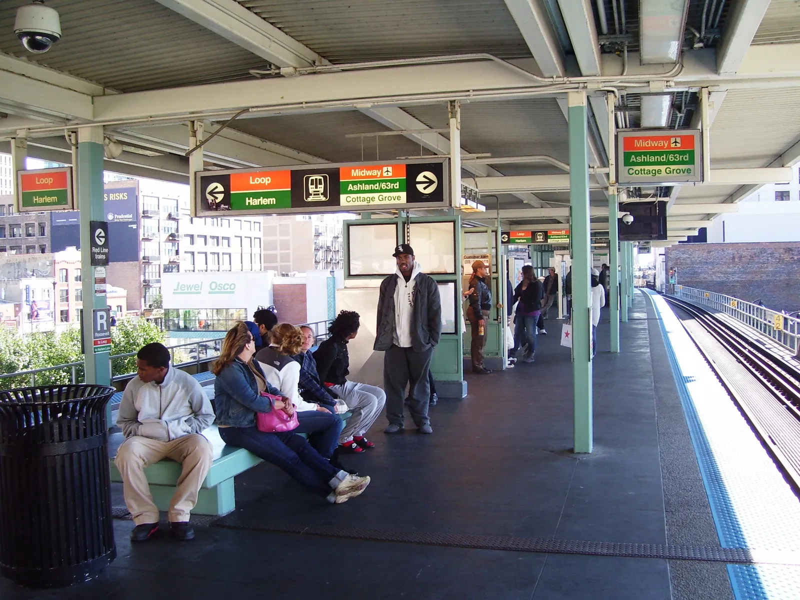 The elevated platform at Roosevelt station in Chicago, passengers waiting on benches under a canopy with overhead direction signs for the Loop, Harlem, Midway and Ashland