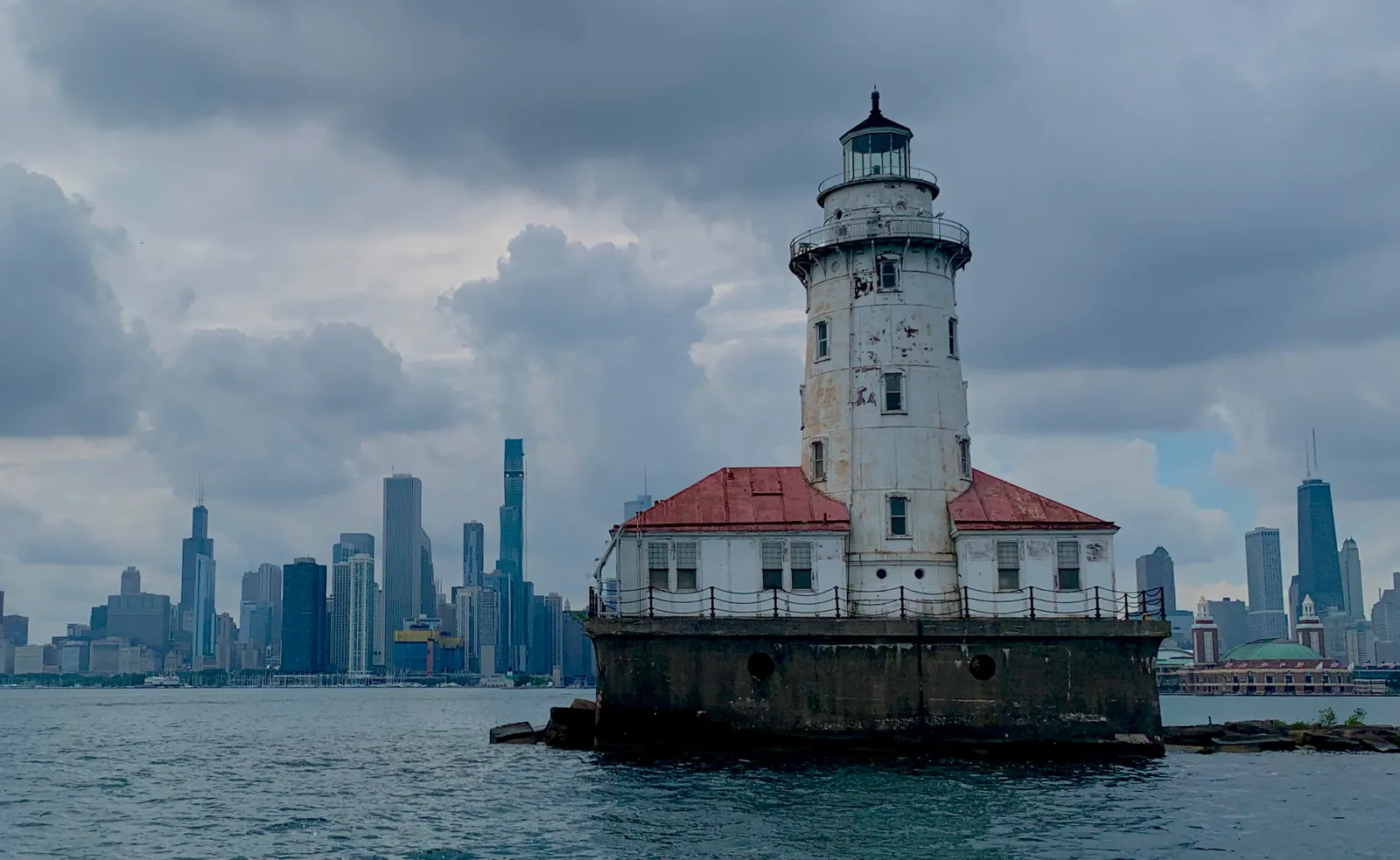 The Chicago Harbor Lighthouse on its breakwater platform, a white tower with a red roof, with the downtown Chicago skyline low on the horizon behind it