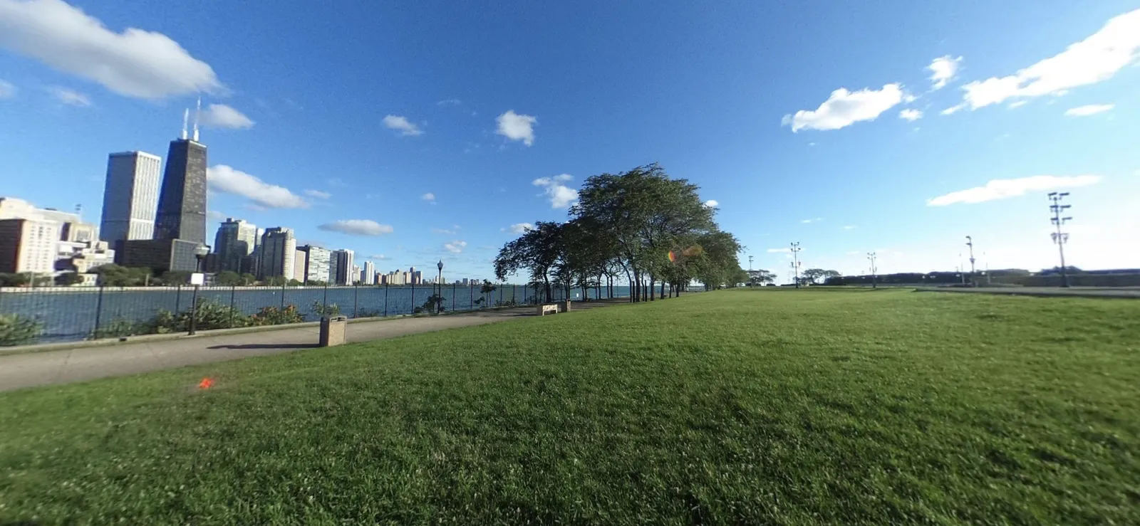 The open lawn of Milton Lee Olive Park on Chicago's lakefront, with trees along the water's edge and the towers of Streeterville and the John Hancock Center to the west