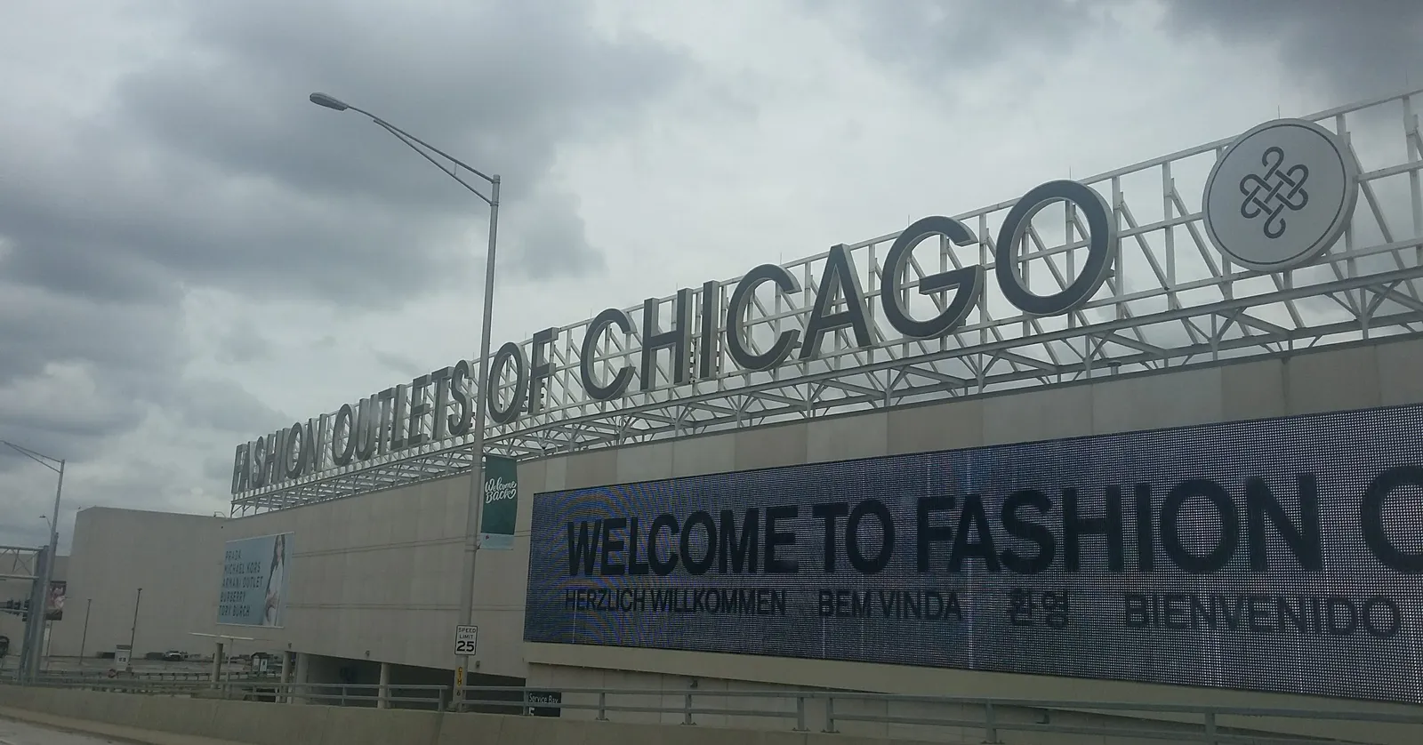 The steel lettering reading Fashion Outlets of Chicago along the roofline of the mall in Rosemont, above a long digital screen carrying a welcome message in several languages