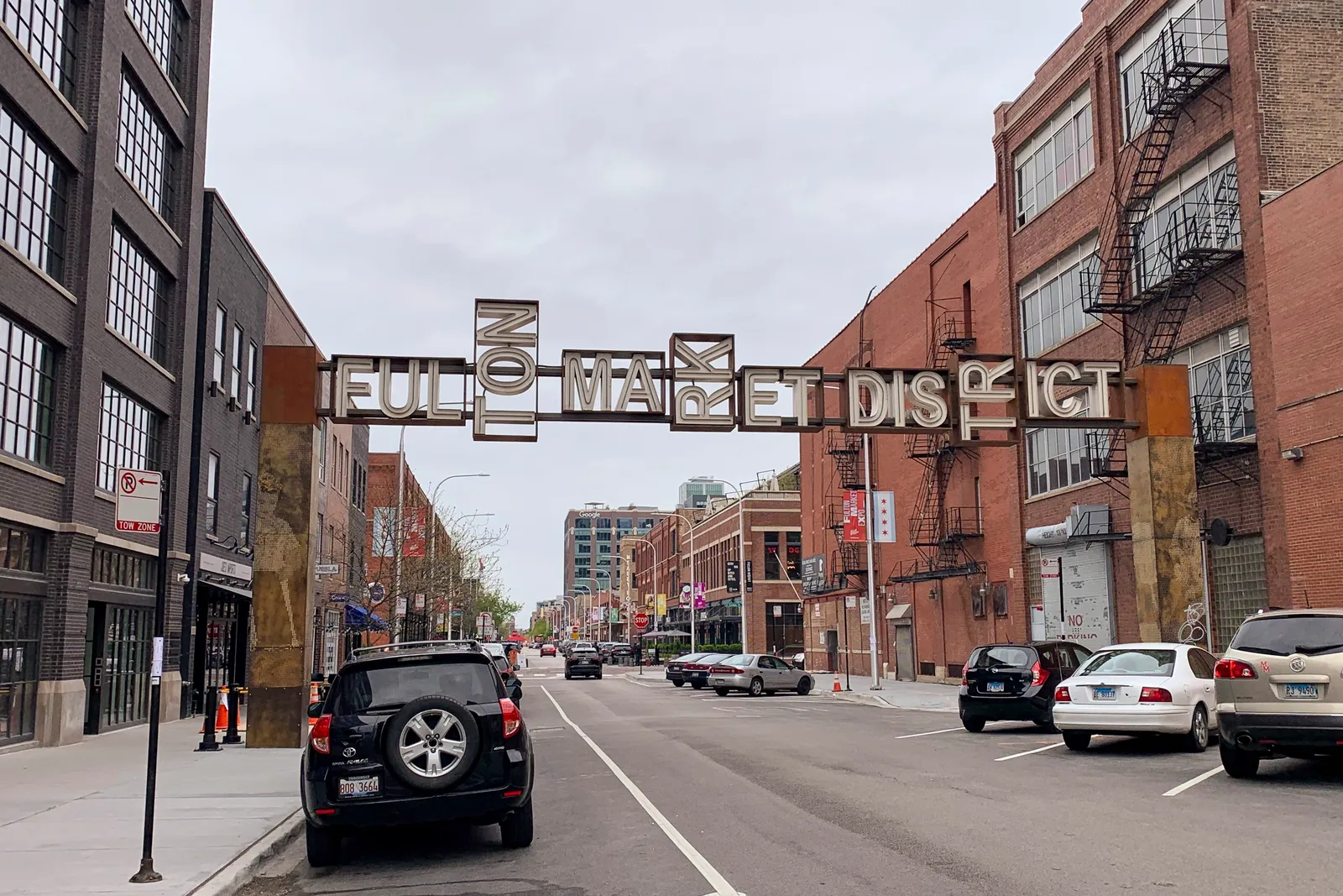 The steel gateway sign reading Fulton Market District arching over a street of brick warehouse buildings in Chicago's West Loop