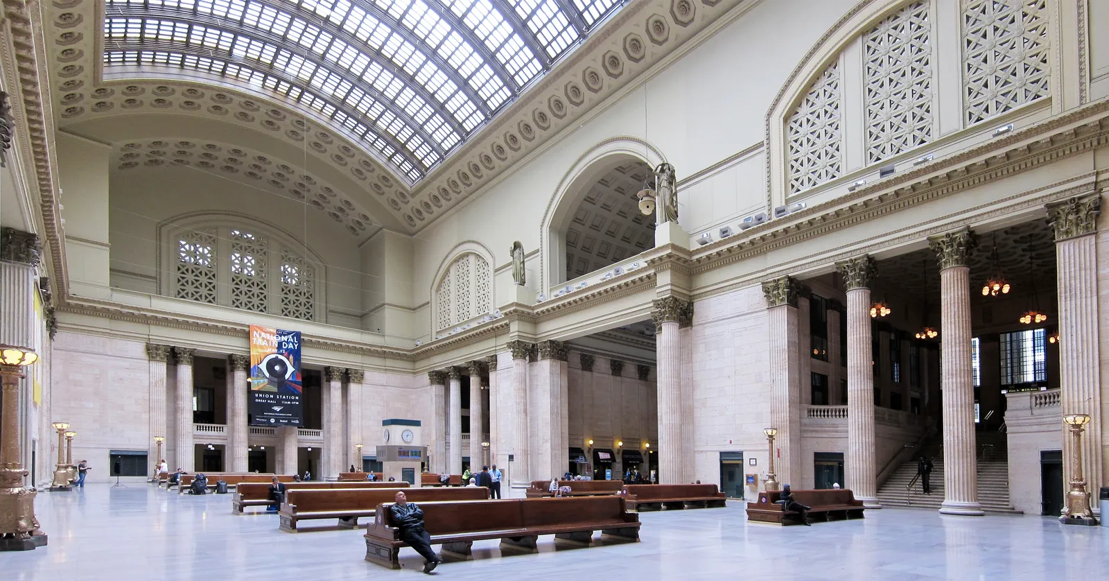 The Great Hall of Chicago Union Station, a marble waiting room lined with Corinthian columns under a long barrel-vaulted glass skylight, with wooden benches on the floor below
