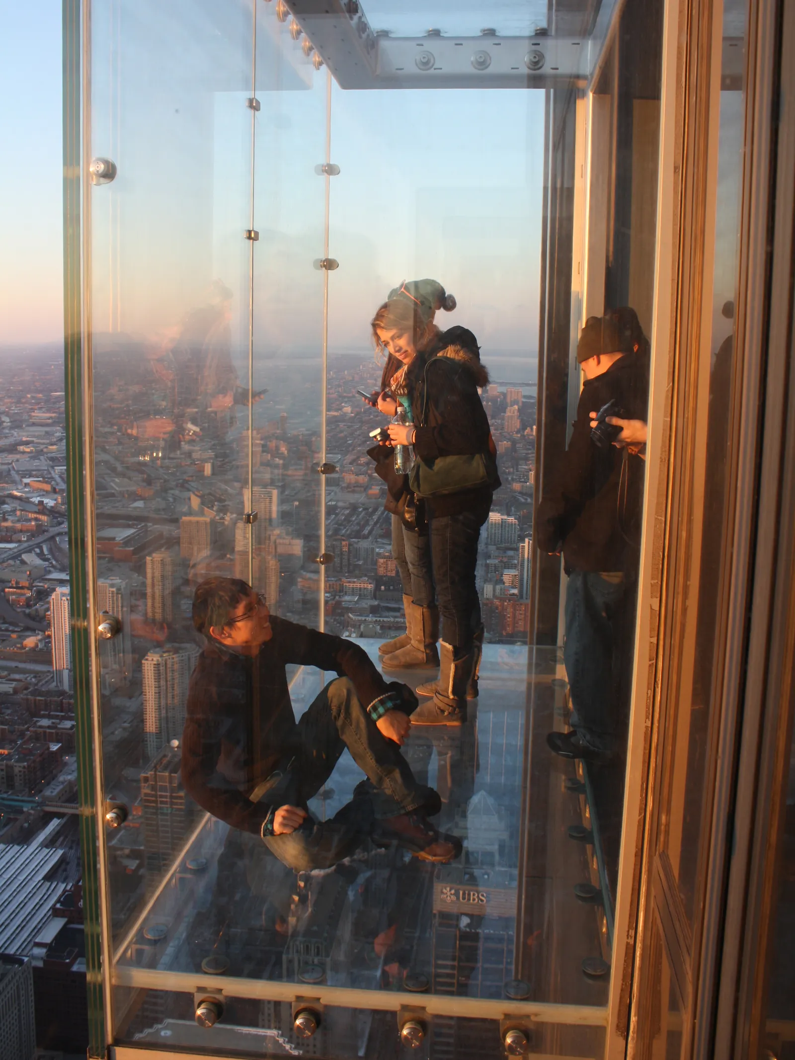 Visitors standing inside a glass box cantilevered off Willis Tower's Skydeck, looking straight down at the city more than a thousand feet below