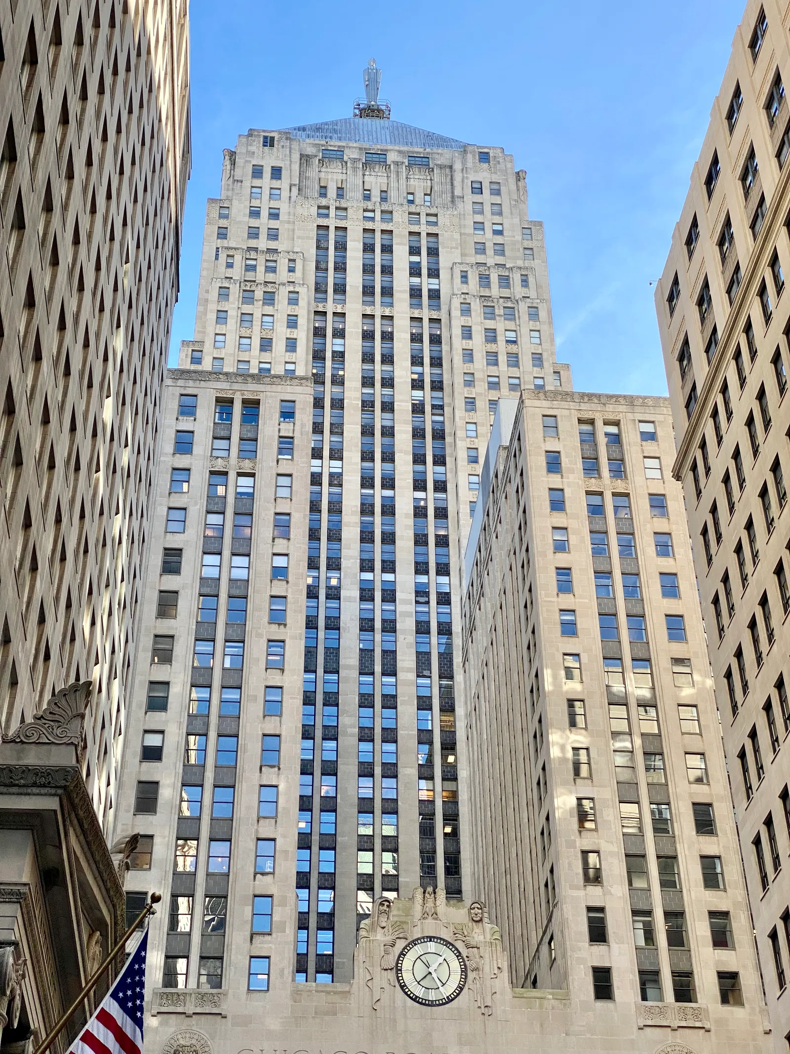 The Chicago Board of Trade Building seen from LaSalle Street, a limestone Art Deco tower stepping back in stages against a blue sky, with its large round clock above the entrance