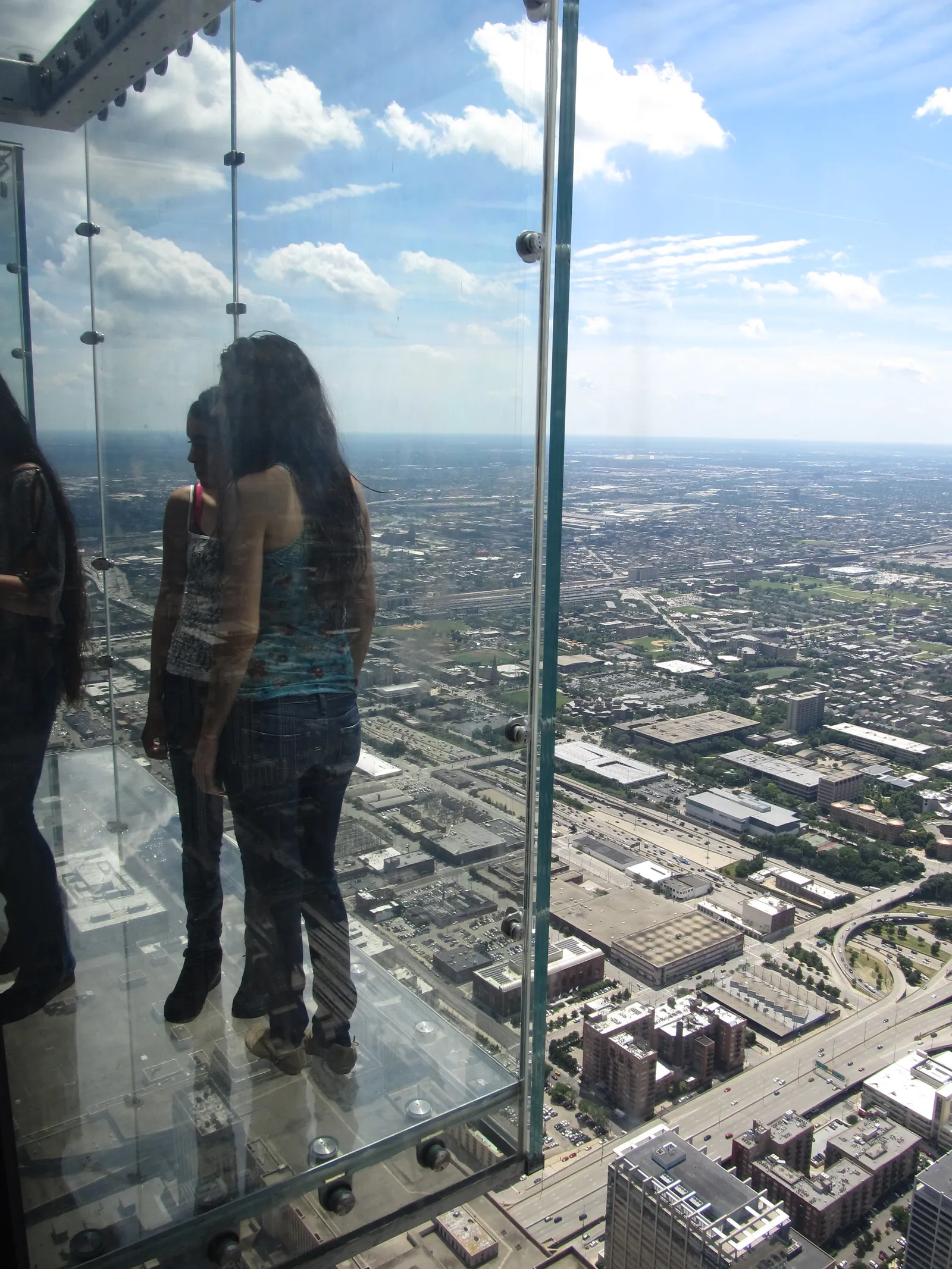 Visitors standing on The Ledge, a glass balcony extending from the Willis Tower Skydeck, with Chicago visible far below
