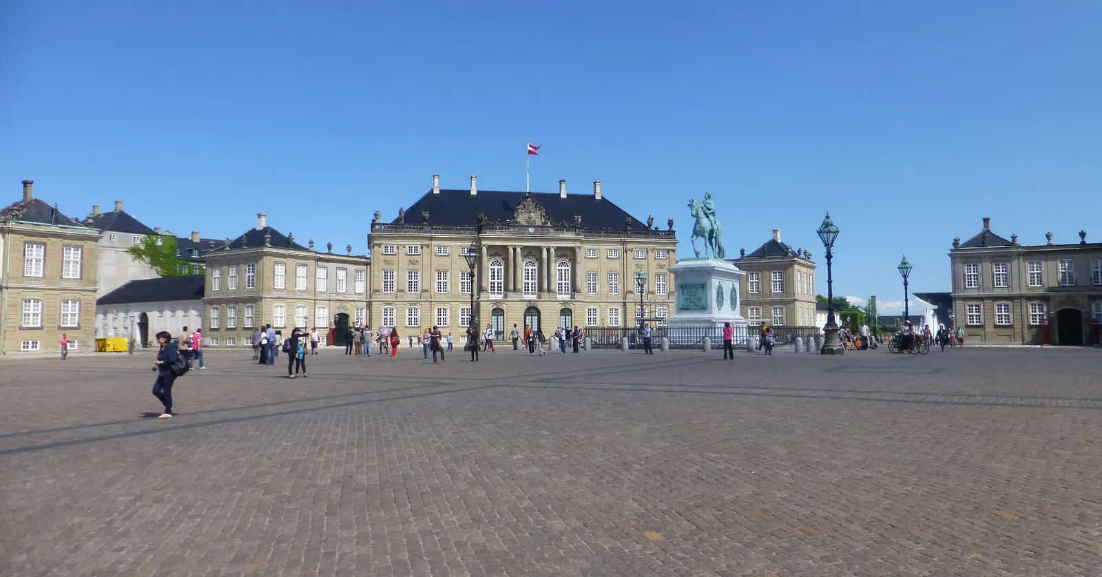 The cobbled octagonal square at Amalienborg in Copenhagen on a sunny day, two matching grey rococo palace wings facing each other across the paving with the bronze equestrian statue of Frederik V between them