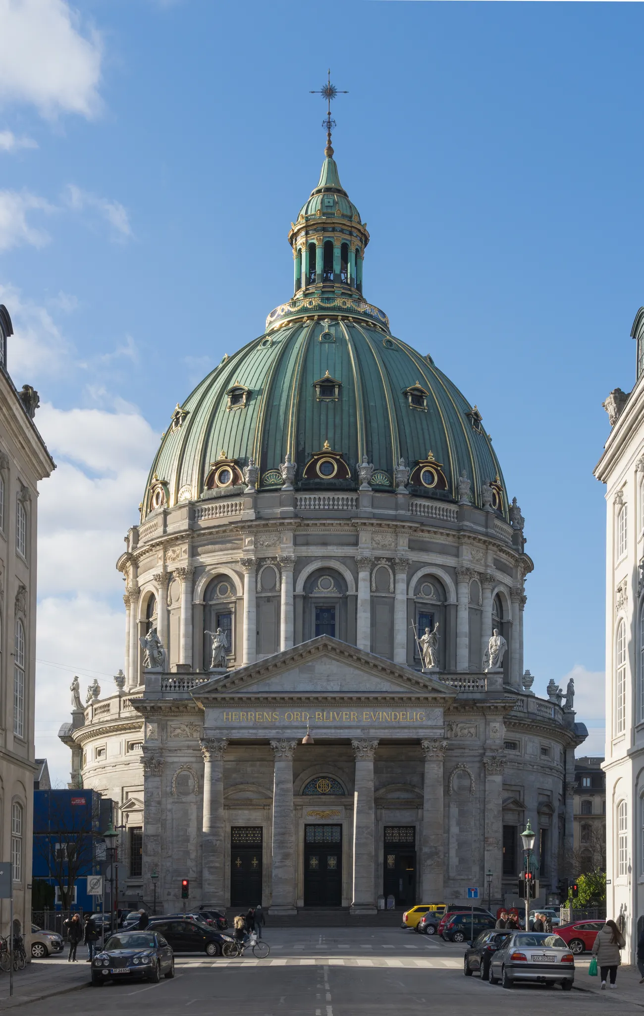 Frederik's Church in Copenhagen seen head-on down a narrow street, a wide green copper dome with gilded ribs and round windows sitting on a pale stone drum above a columned portico