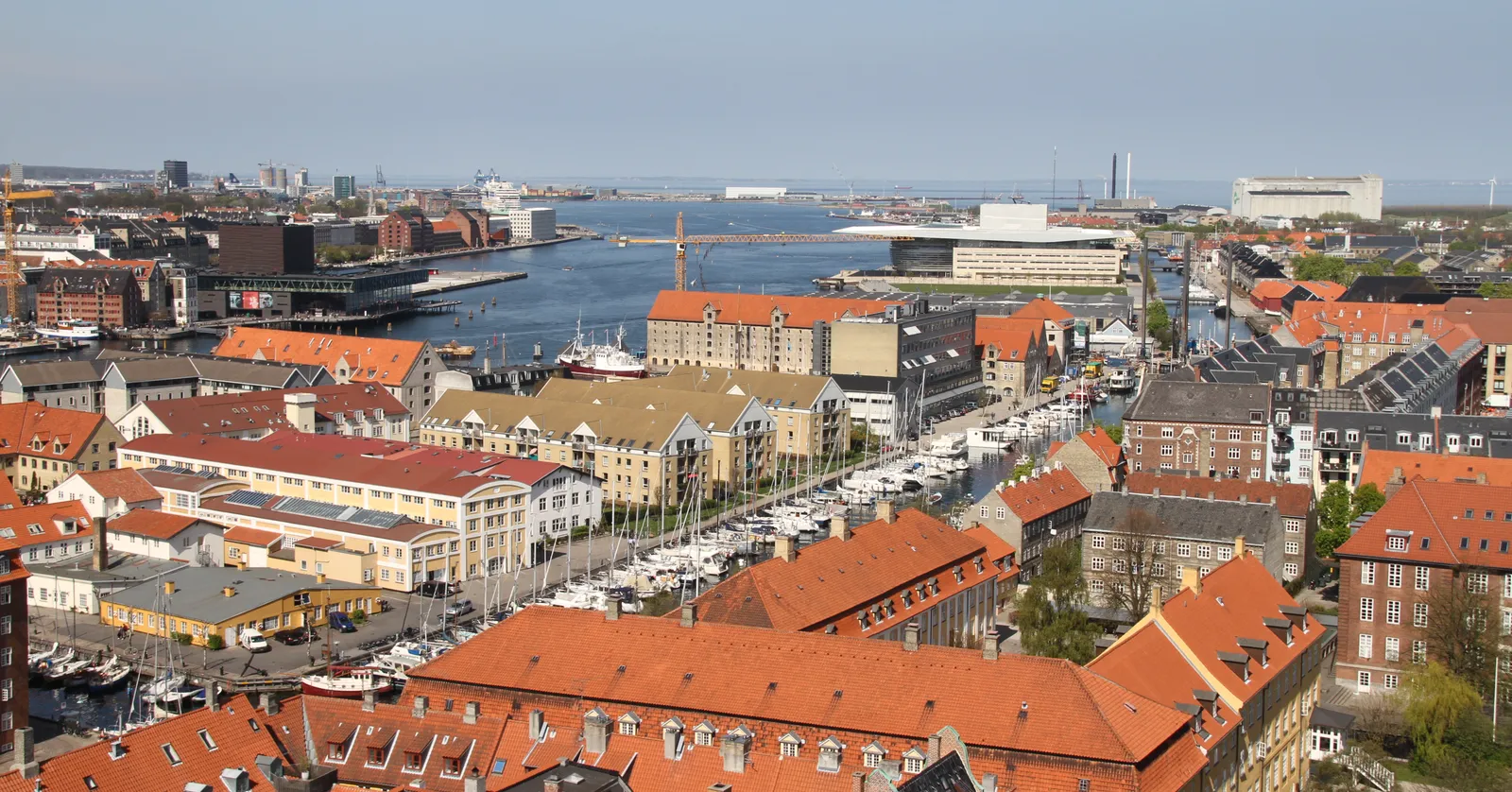 Christianshavn in Copenhagen seen from above, the straight canal running through the middle of the district lined with moored boats, red-tiled roofs on both banks and the harbour opening out beyond