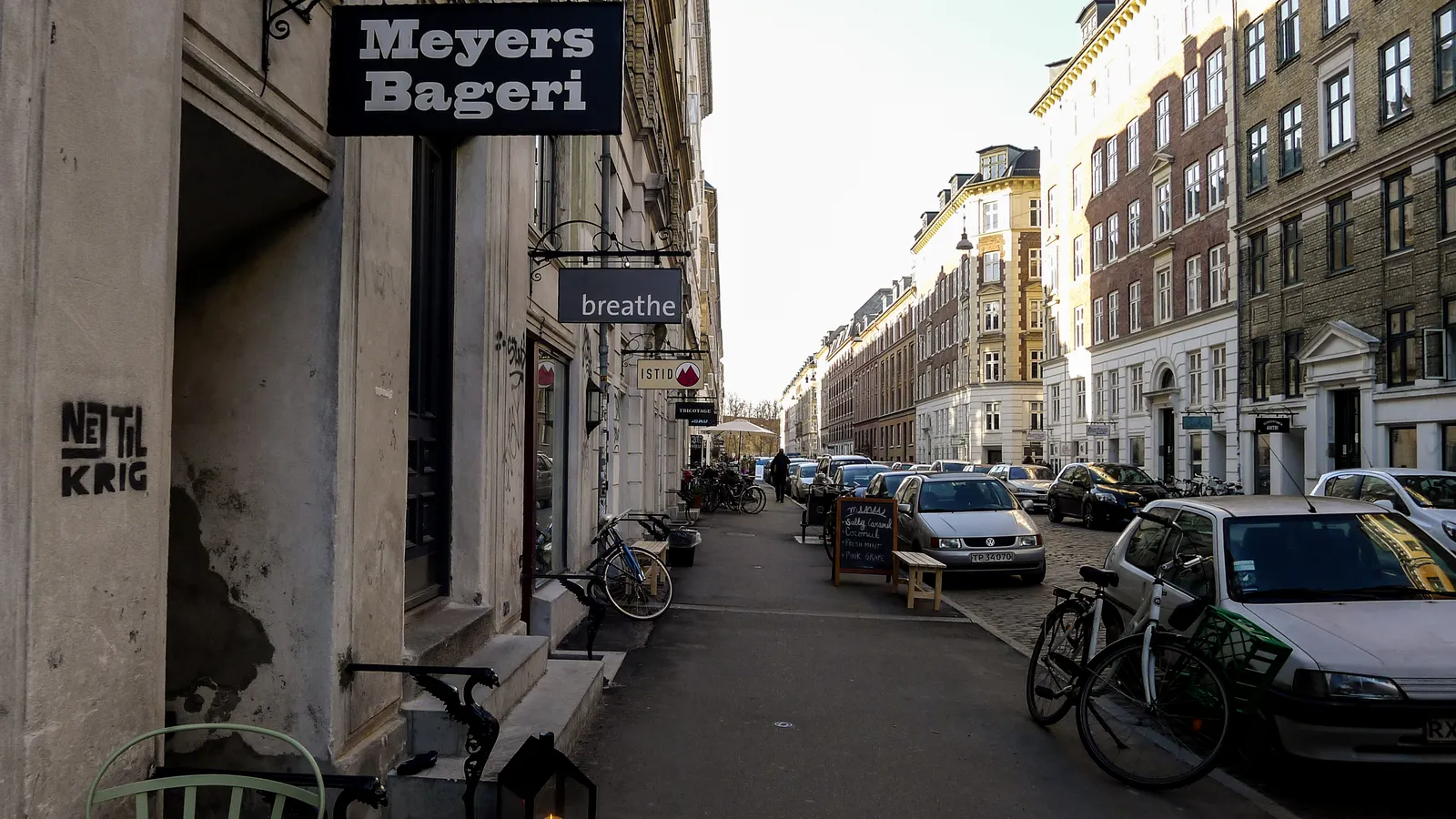 Jægersborggade in Copenhagen's Nørrebro, a narrow residential street with a bakery sign and small shopfronts along the ground floors, bicycles parked against the kerb and five-storey apartment blocks running down both sides