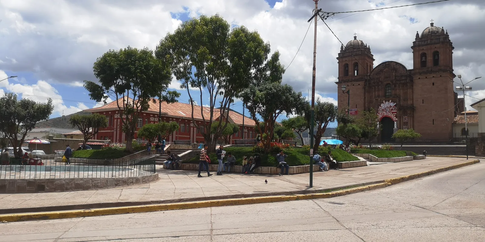 The twin bell towers and stone front of the Belén church in Cusco seen across its small planted plaza, with a low red-roofed building alongside