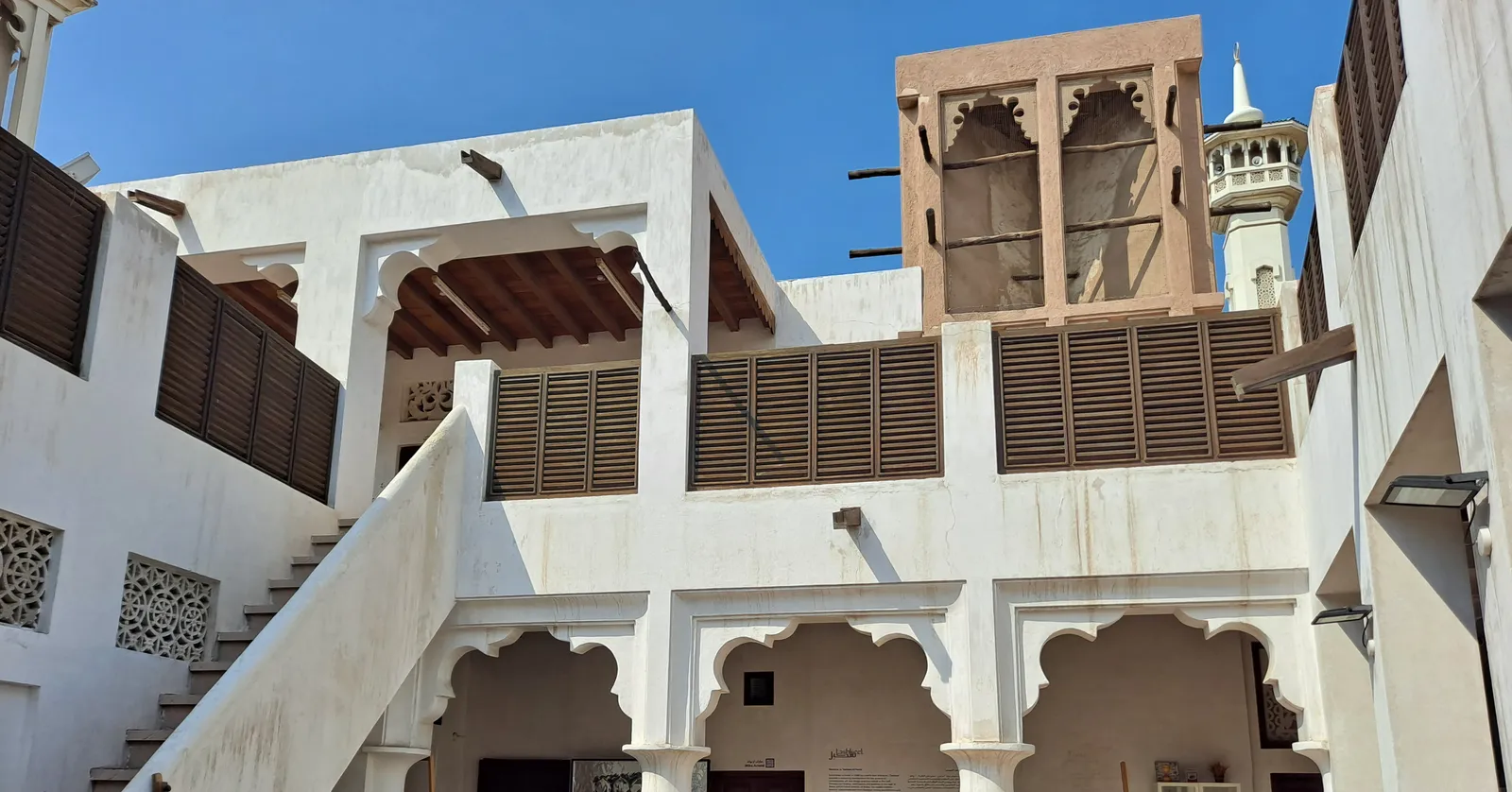 A whitewashed courtyard house in Dubai's Al Fahidi Historical Neighbourhood, with carved arches, wooden shutters and a square wind tower rising above the roofline