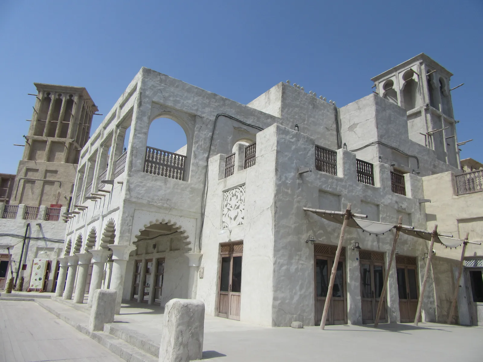 A white two-storey building with arched balconies and two wind towers at Al Seef on the Bur Dubai side of Dubai Creek, under a clear blue sky