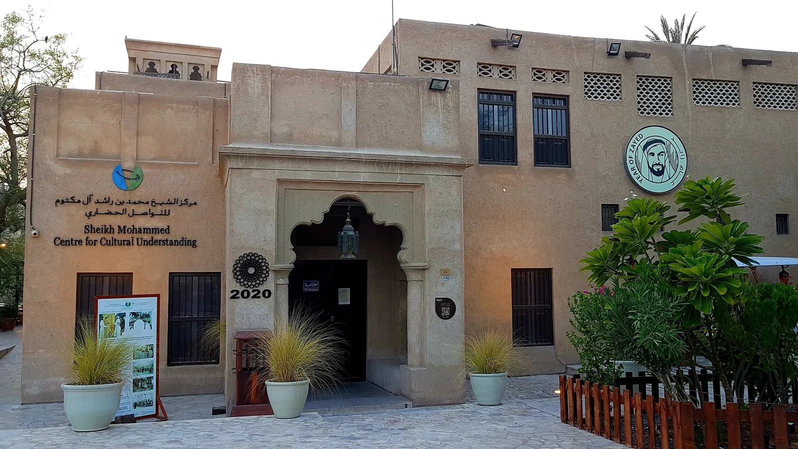 The arched doorway of the Sheikh Mohammed Centre for Cultural Understanding in a sand-coloured house in Al Fahidi, Dubai, with its name in Arabic and English beside the entrance