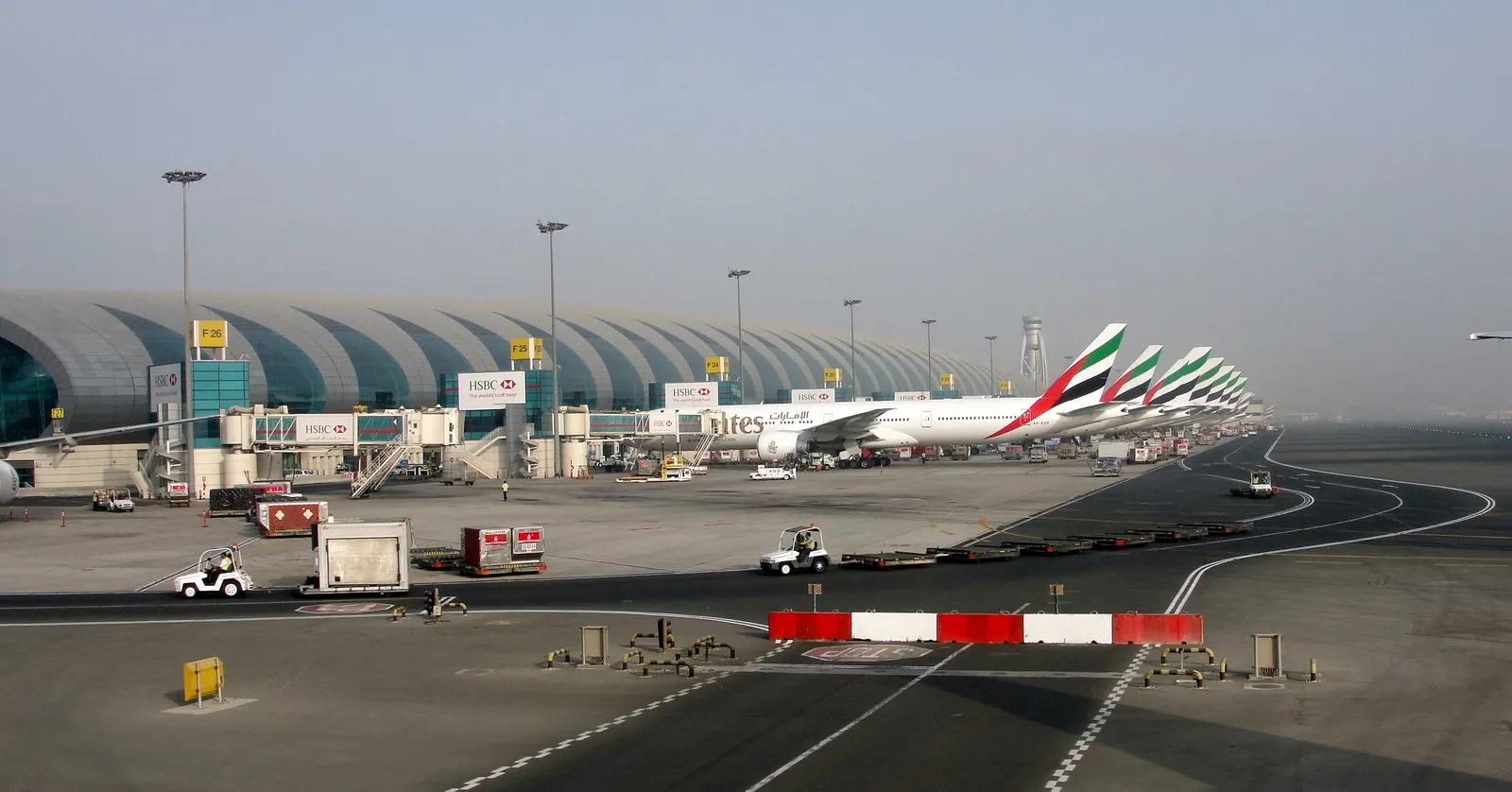 The long curved roof of Terminal 3 at Dubai International Airport, with a row of Emirates aircraft parked nose-in along the concourse