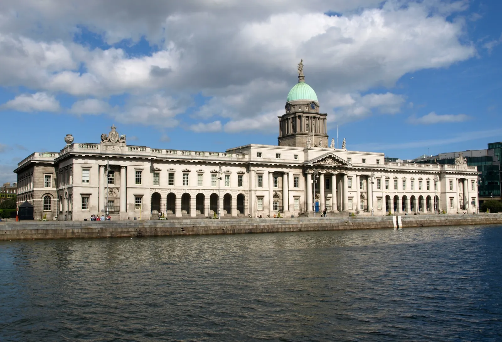 The Custom House in Dublin seen from across the River Liffey, a long pale stone front of arcades and columns with a green copper dome and statue rising over its central portico