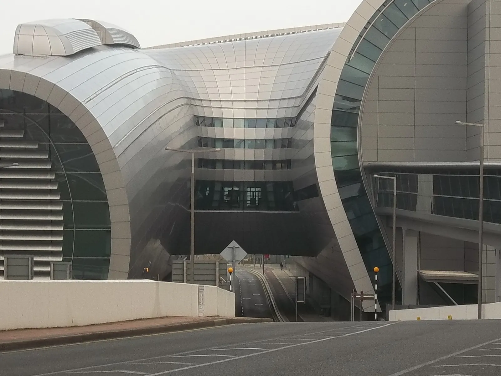 Terminal 2 at Dublin Airport from the approach road, a long curved shell of ridged metal cladding sweeping down to a glazed front with the terminal's inner floors visible through it