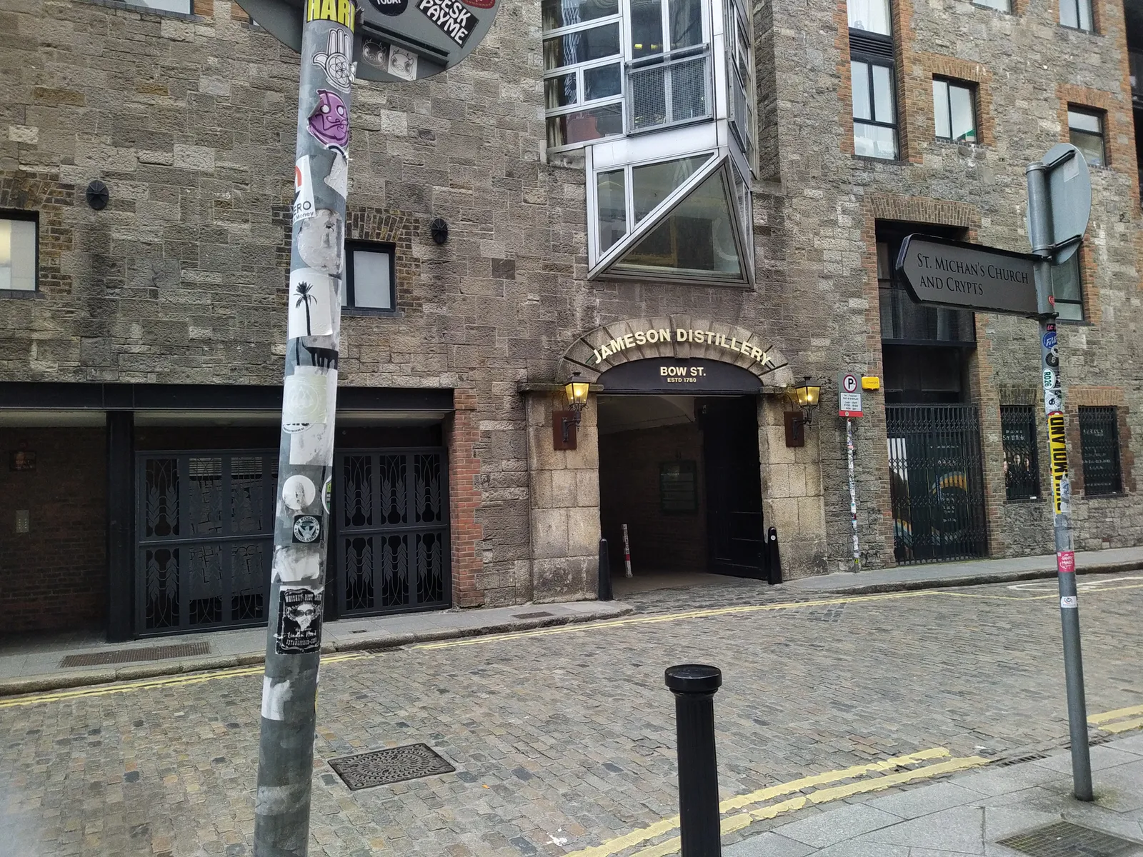 The Bow Street entrance to the Jameson distillery in Dublin, an arched doorway in a dark stone warehouse wall lettered Jameson Distillery Bow St, with a cobbled street running past it