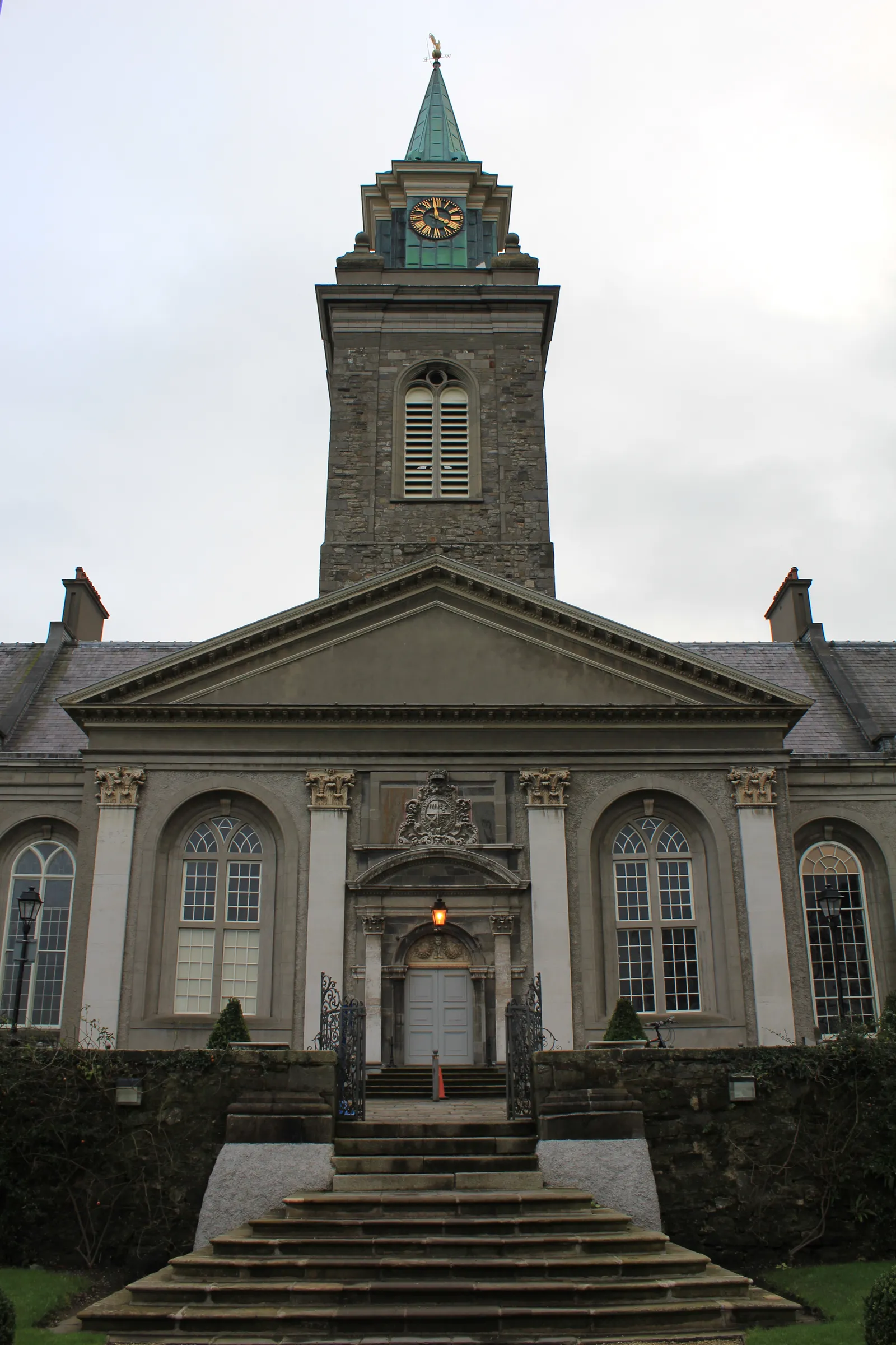 The front of the Royal Hospital Kilmainham in Dublin, a grey stone portico under a pediment with a tall clock tower and green copper spire rising behind it, reached by a flight of steps