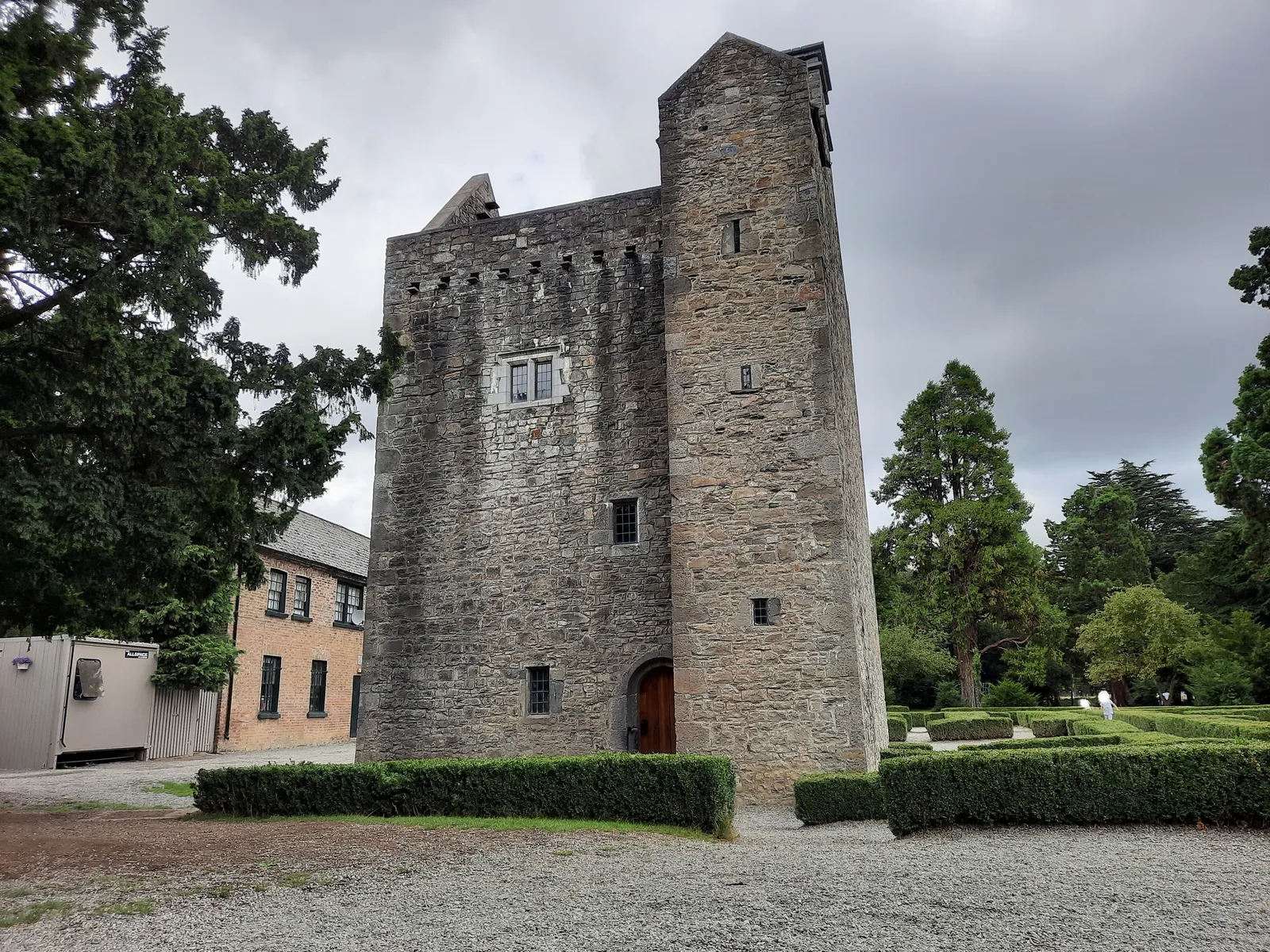 Ashtown Castle in Dublin's Phoenix Park, a tall square grey stone tower house with a steep gable and a stair turret, standing behind clipped hedges on a gravel forecourt