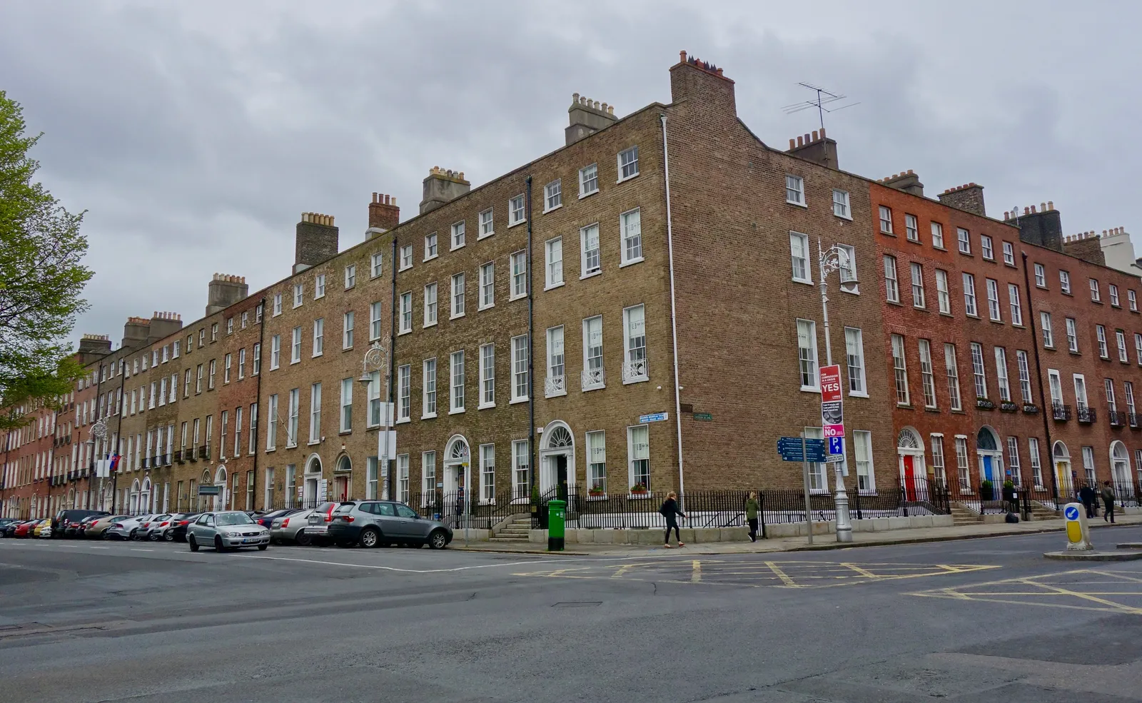 A corner of Merrion Square in Dublin, four storeys of red and brown Georgian brick running the length of the street with rows of chimneys along the roofline and cars parked below