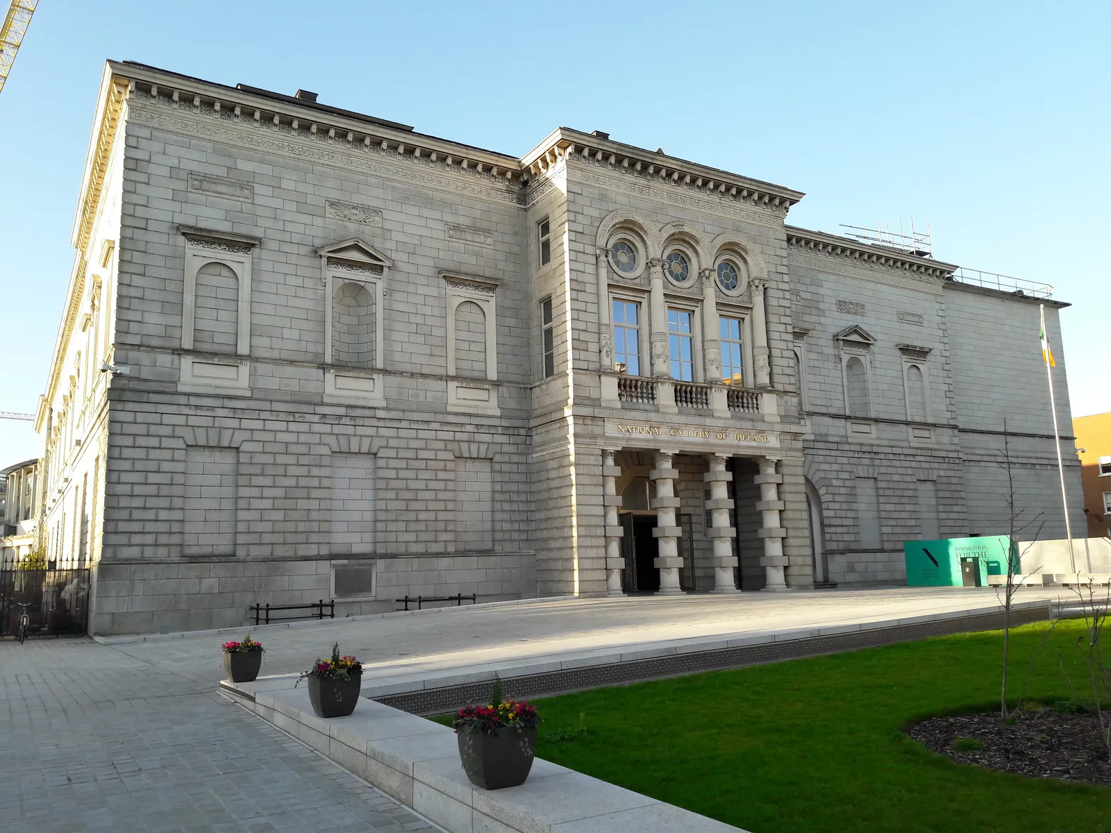 The National Gallery of Ireland in Dublin, a long pale stone front with a columned porch under an arcaded first-floor window, seen across its forecourt in evening light
