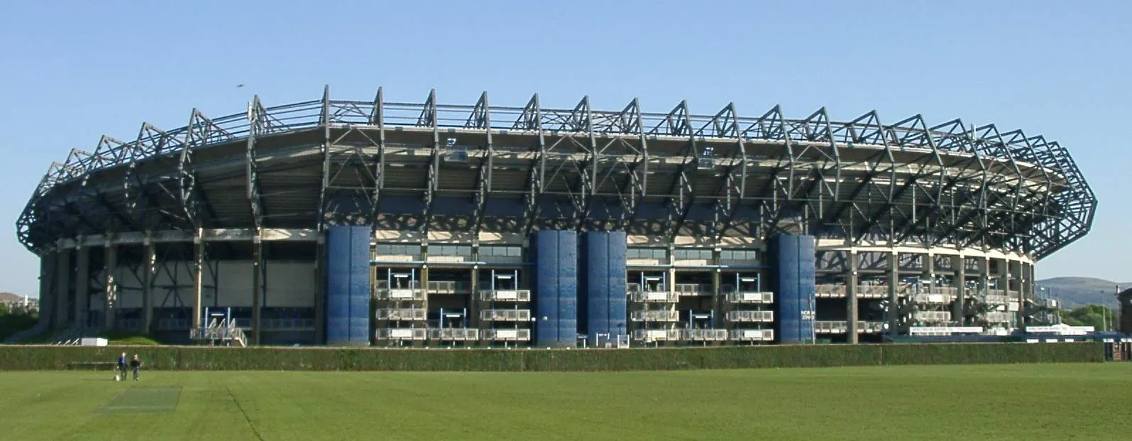 The long steel-roofed west stand of Murrayfield Stadium in Edinburgh seen across an open playing field on a clear day
