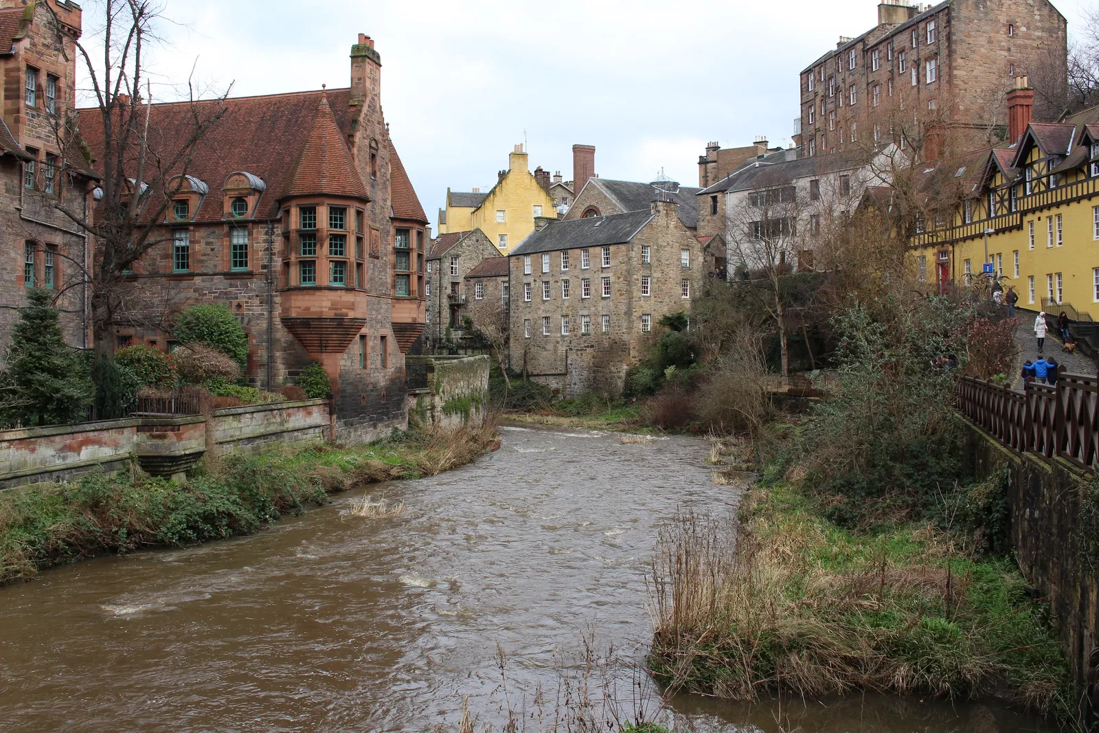 The Water of Leith running through Dean Village in Edinburgh, with the red-tiled Well Court tenement on the left bank and pale stone mill houses stepping down to the water
