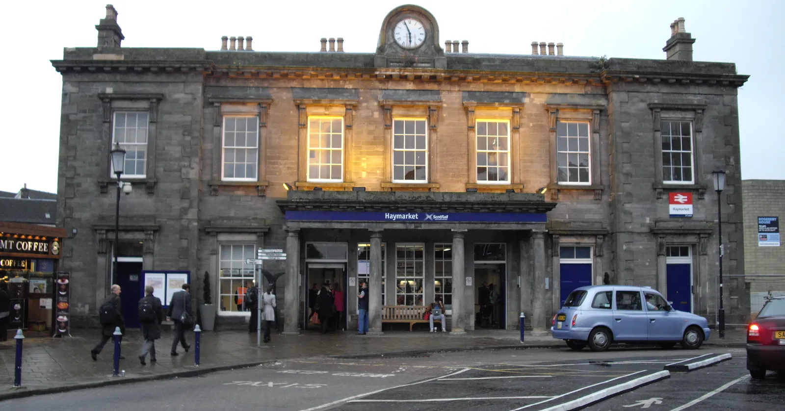 The 1842 Georgian frontage of Haymarket station in Edinburgh, a low pale sandstone building with a clock over its central bay, lit against a grey afternoon