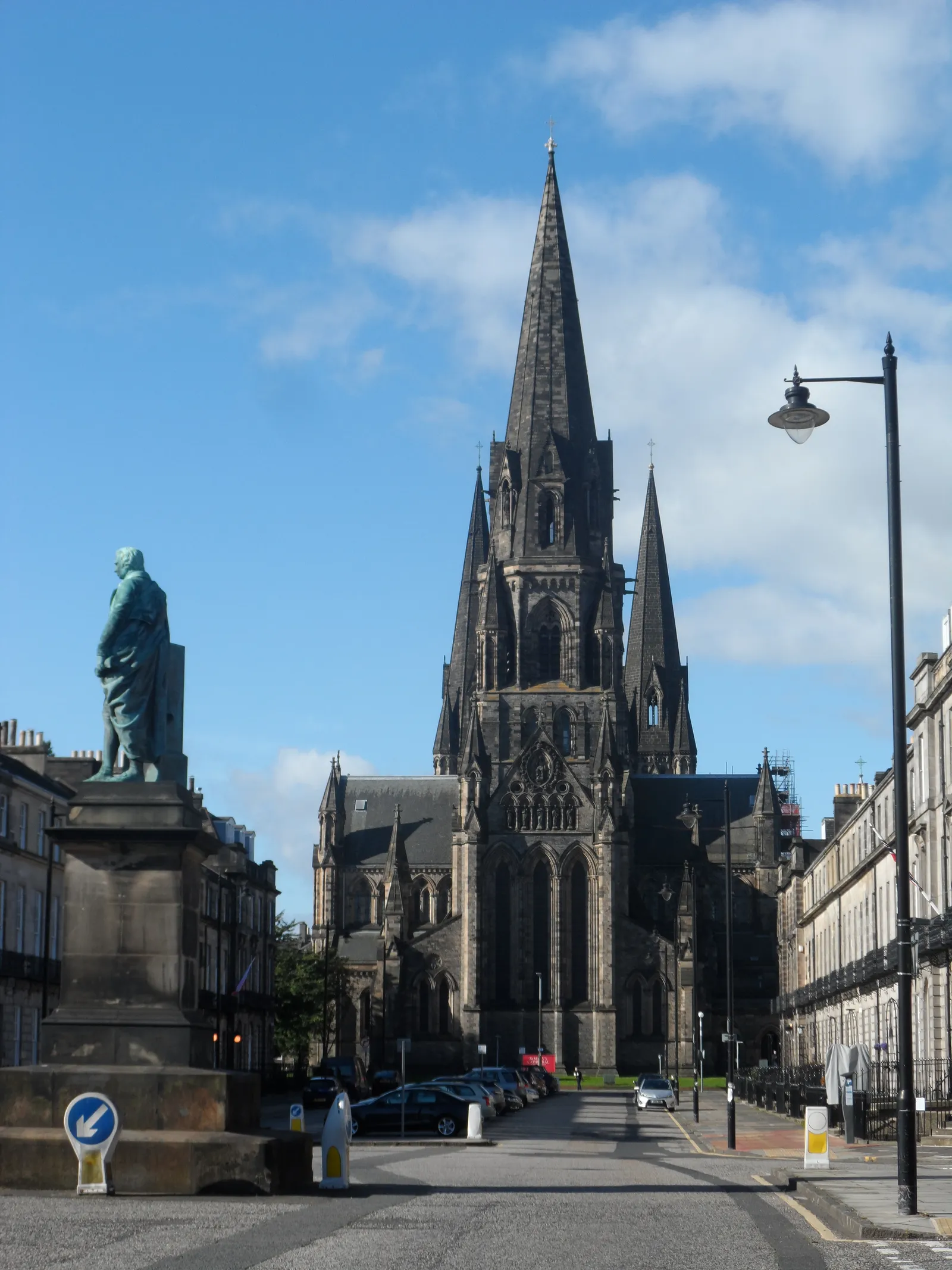 St Mary's Episcopal Cathedral in Edinburgh's West End seen down Melville Street, its tall central spire flanked by two smaller ones against a blue sky