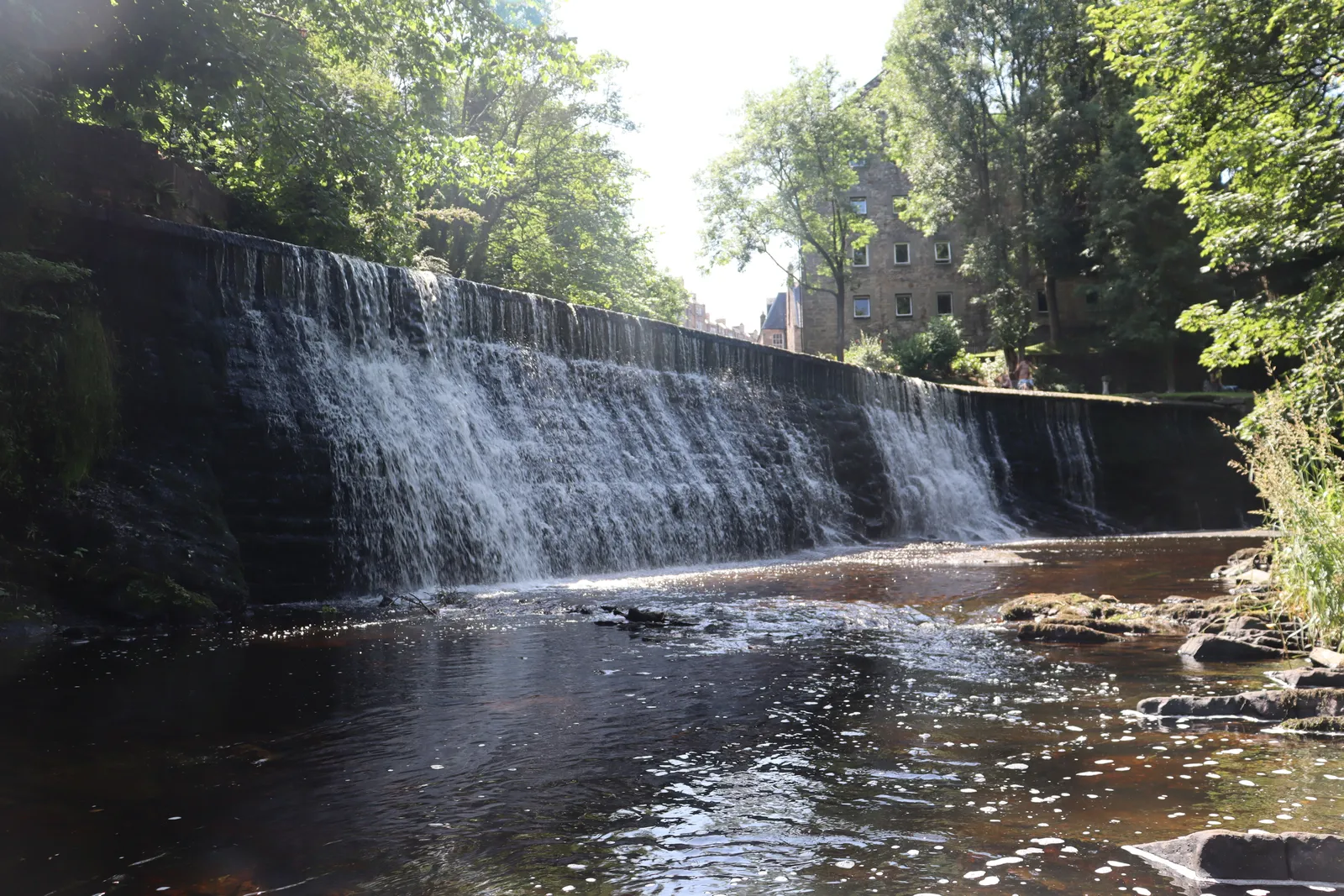 A weir on the Water of Leith running through Dean Village, Edinburgh, framed by trees and old mill buildings
