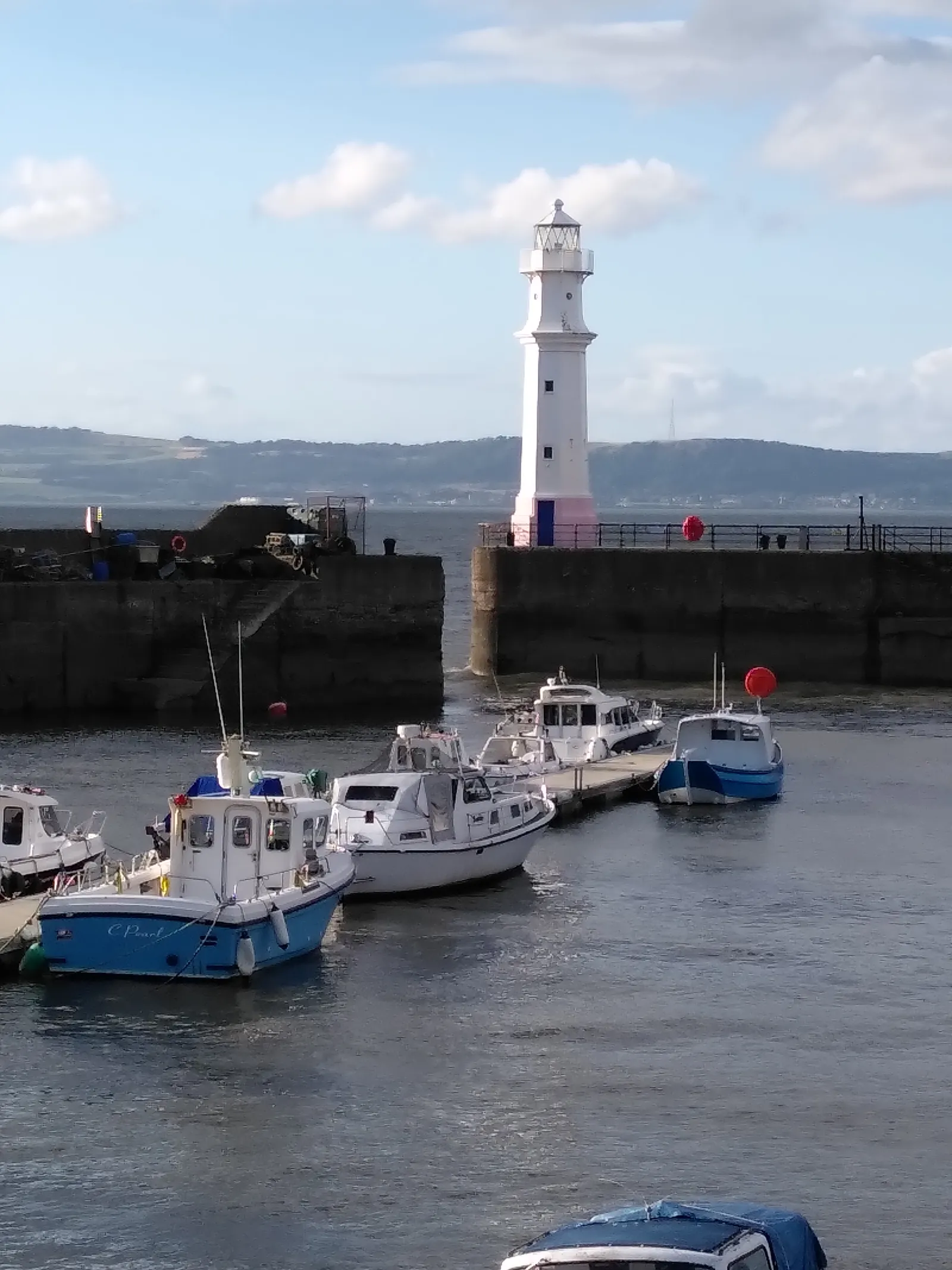 Newhaven harbour in Edinburgh, small fishing and pleasure boats moored inside a stone breakwater with a white lighthouse standing at its end