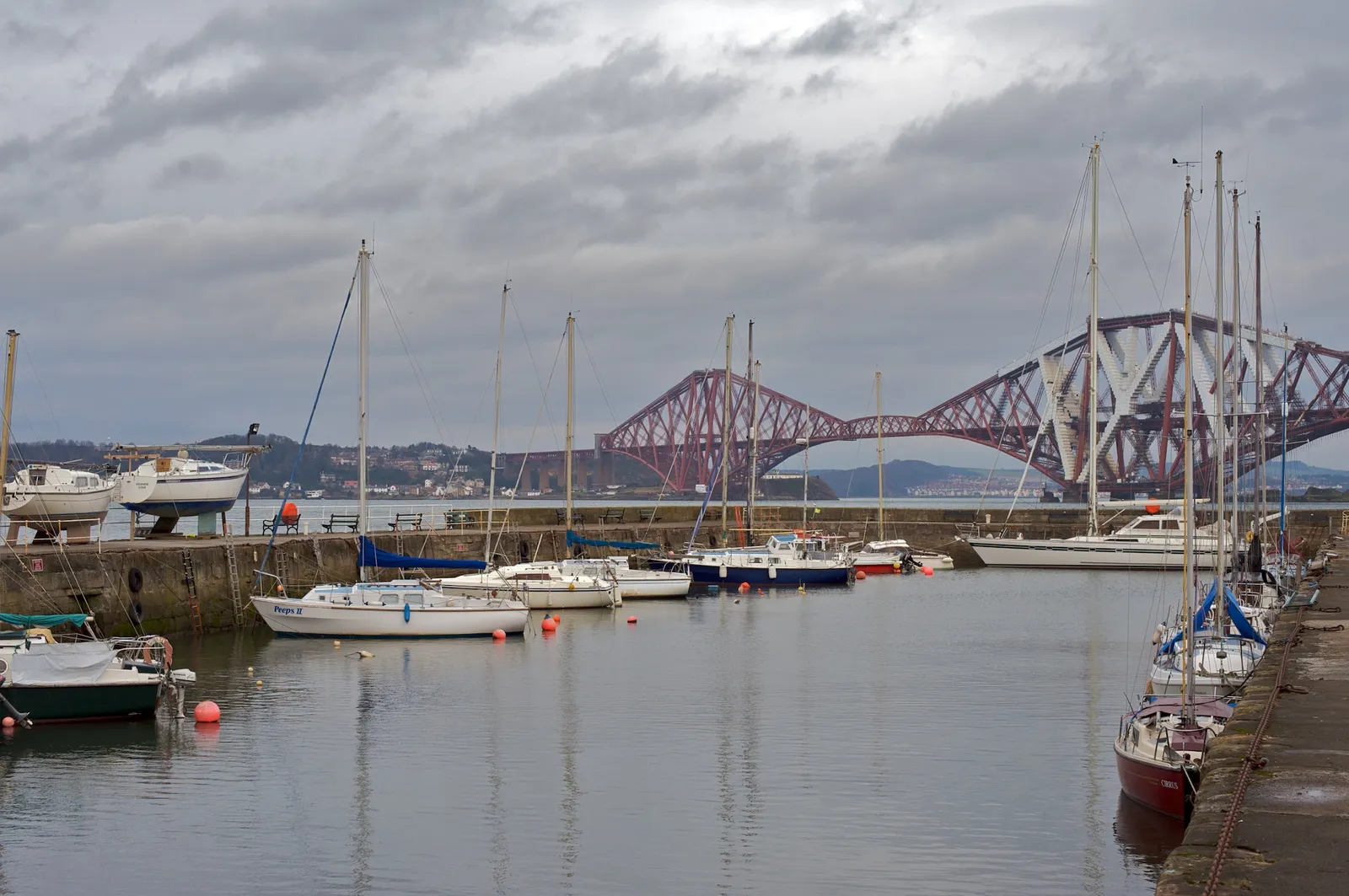 Sailboats moored in South Queensferry harbour with the red Forth Bridge visible across the water