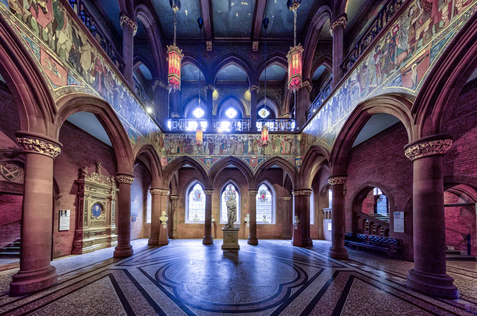 The Great Hall of the Scottish National Portrait Gallery in Edinburgh, red sandstone arcades under a painted frieze of figures and a deep blue starred ceiling