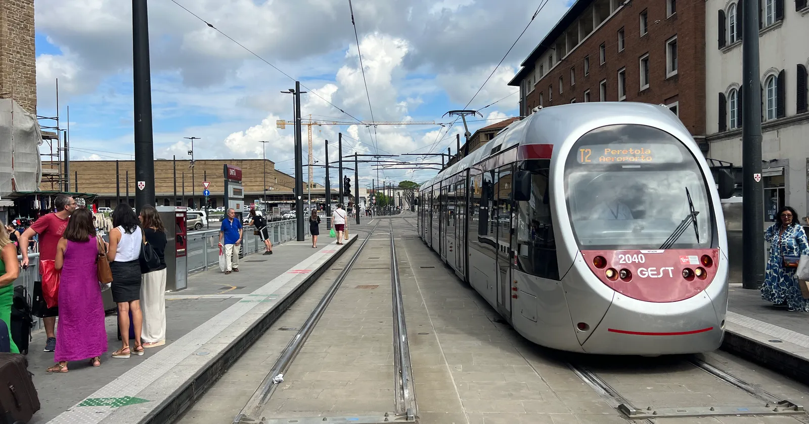 A silver T2 tram at the Unità stop beside Santa Maria Novella station in Florence, the end of the line from the airport, with passengers on the platform