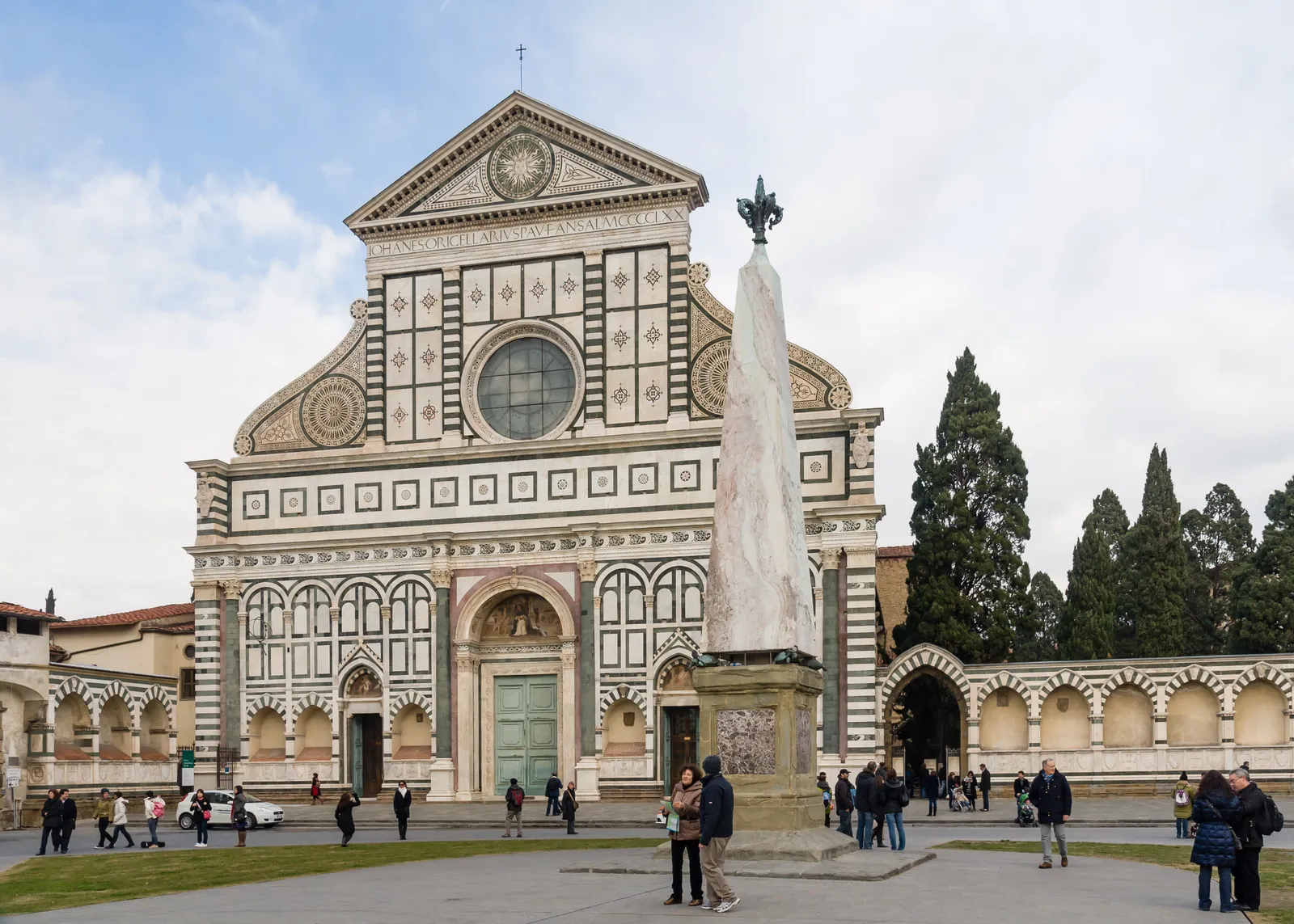 The green and white marble geometric facade of the Basilica di Santa Maria Novella with its piazza obelisk in Florence