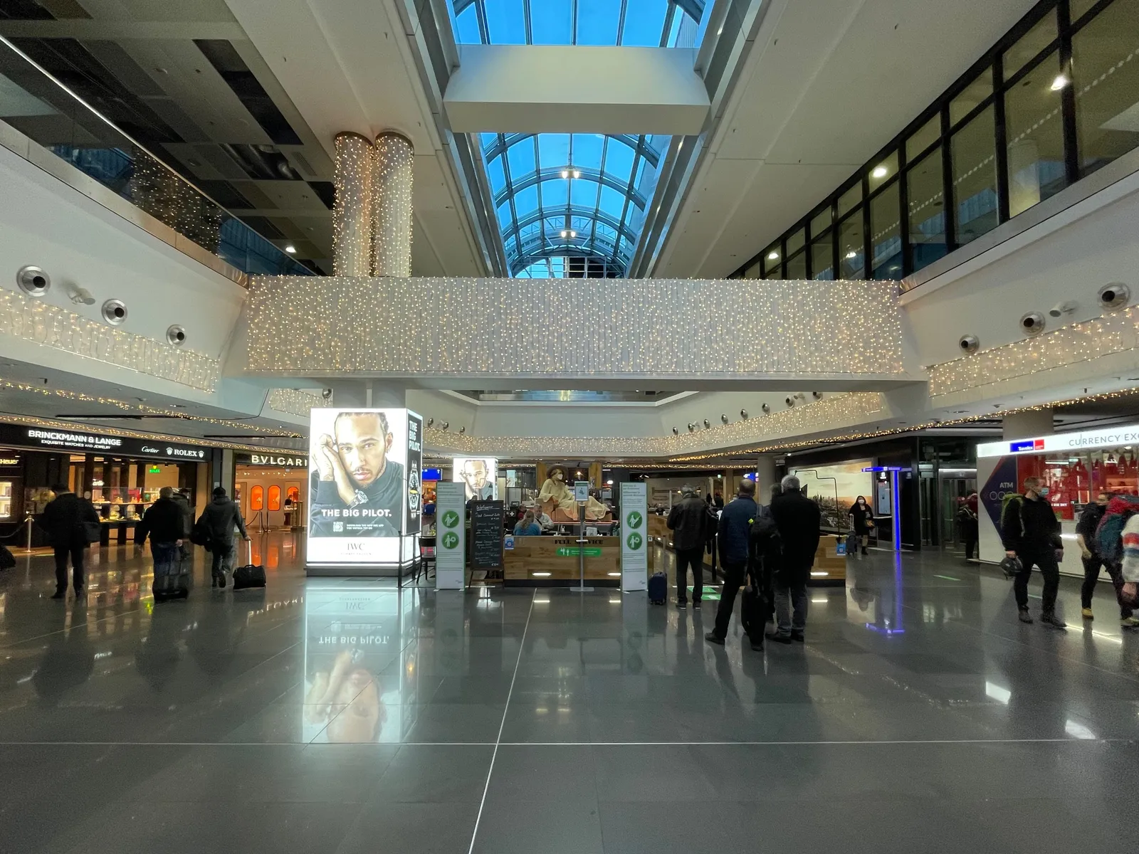 The non-Schengen shopping concourse of Frankfurt Airport's Terminal 1, a glass-roofed hall lined with duty-free shops and travelers walking between them