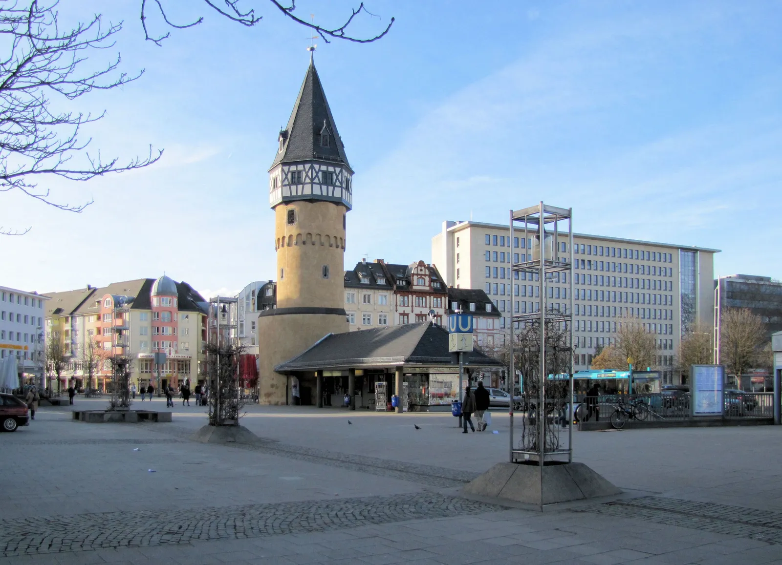The Bockenheimer Warte, a stone medieval watchtower with a half-timbered upper section and pointed roof, standing in an open plaza above a U-Bahn entrance